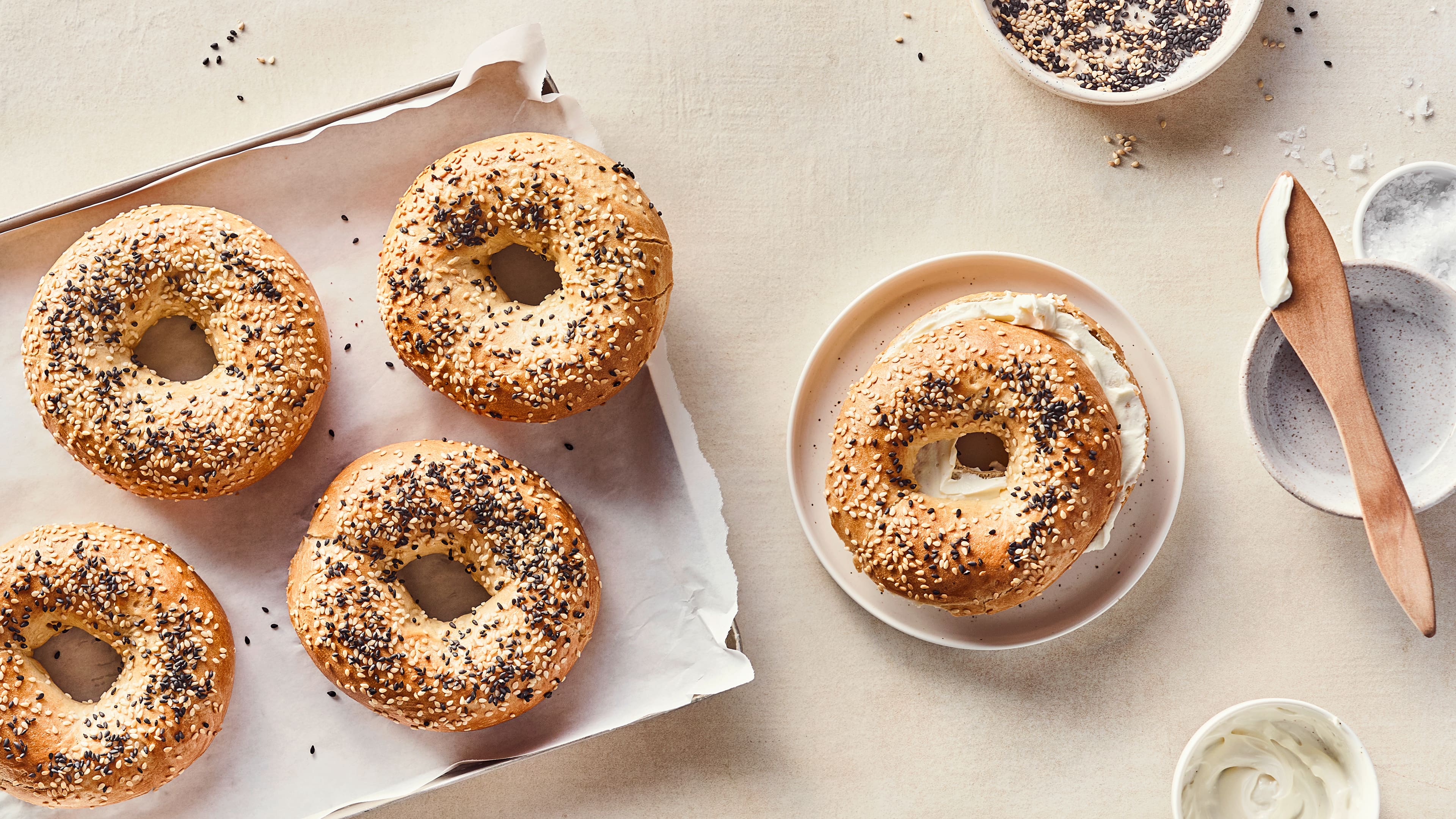 Rezept für Protein Bagels Gelbgold gebacknene Bagel mit weißem und schwarzem Sesam und cremigem Frischkäse, auf einem runden Teller