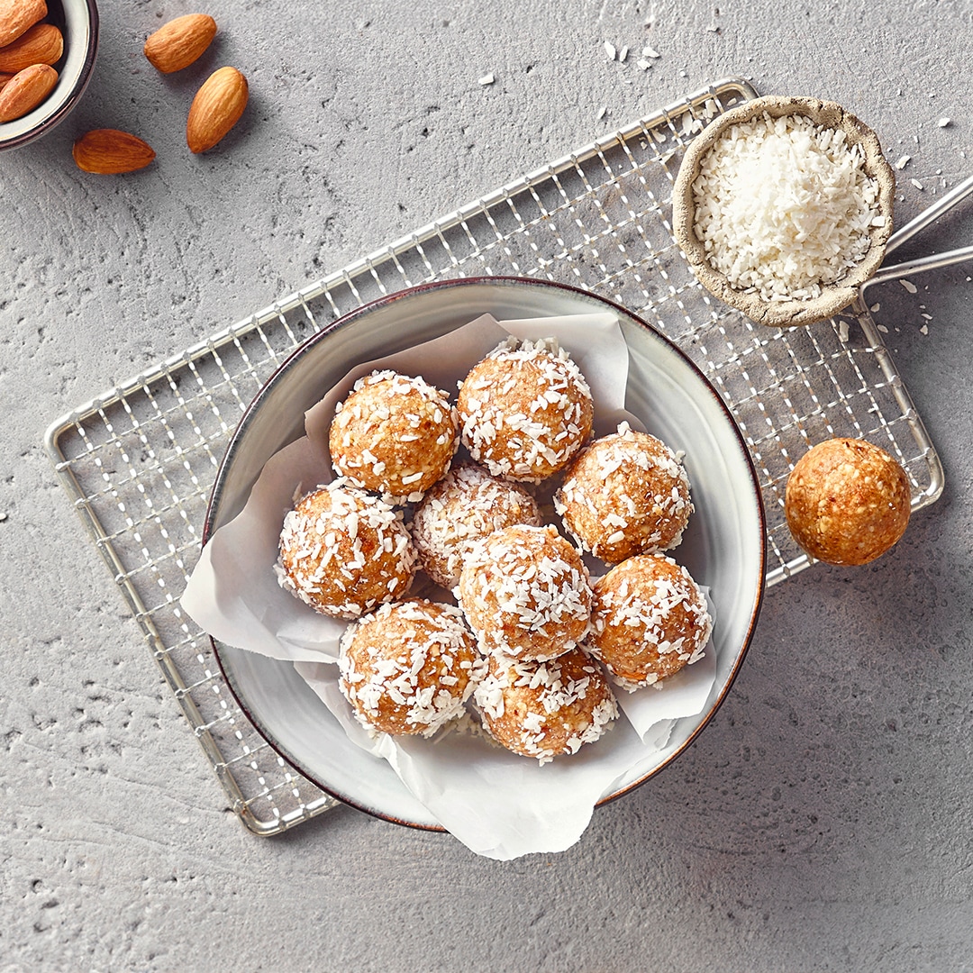 Eine Schale mit goldbraunen Kugeln aus Mandeln und Datteln, garniert mit feinen weißen Kokosraspeln