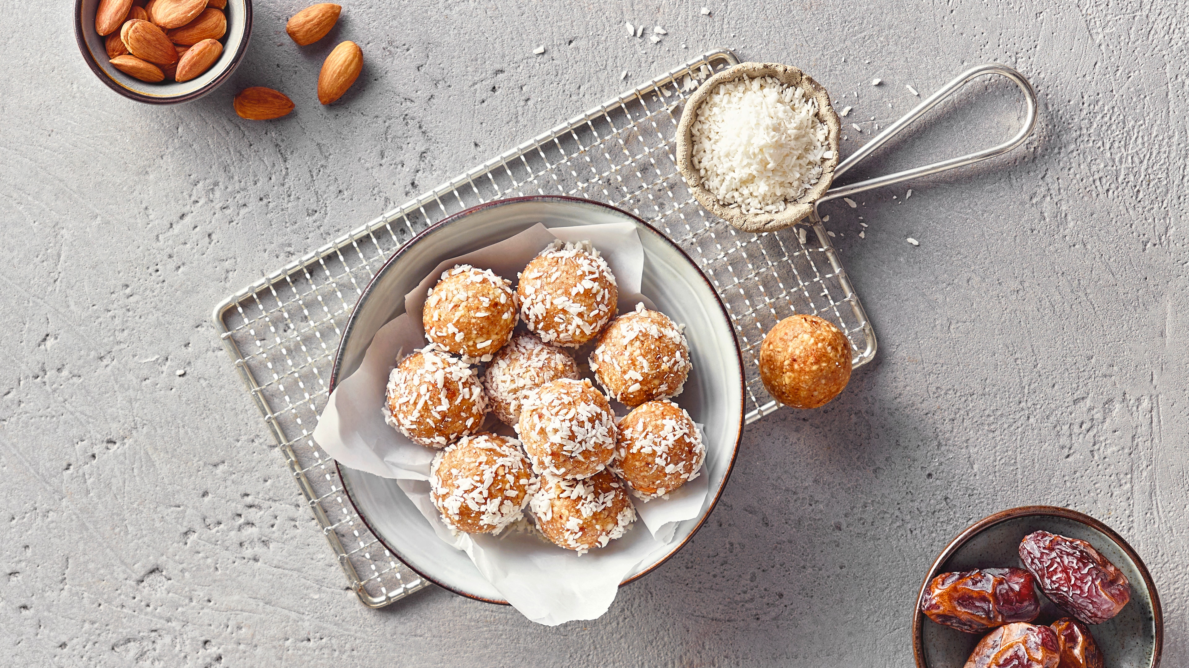 Eine Schale mit goldbraunen Kugeln aus Mandeln und Datteln, garniert mit feinen weißen Kokosraspeln