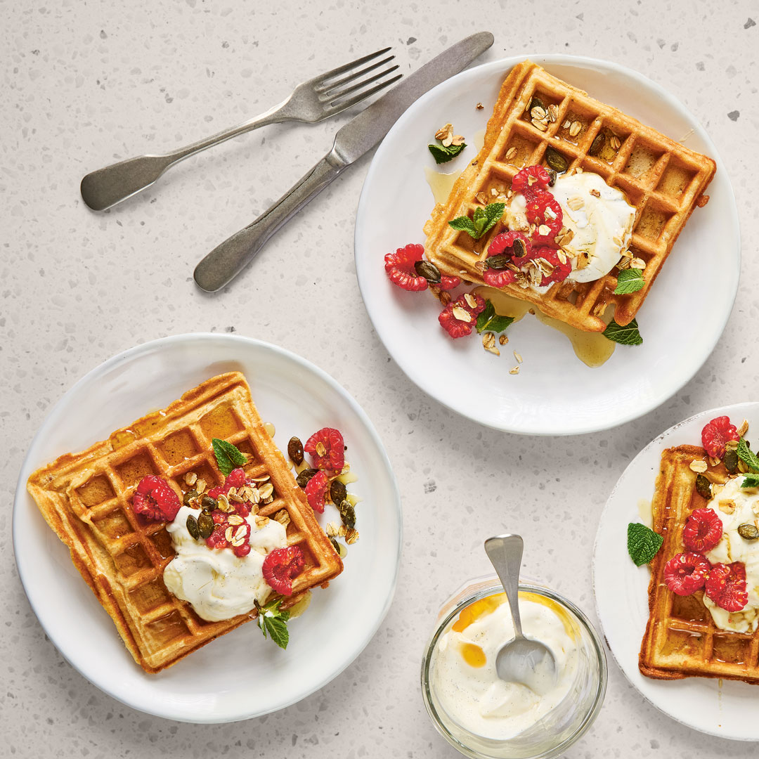 Drei Teller mit jeweils einer Waffel, etwas heller Creme und Himbeeren