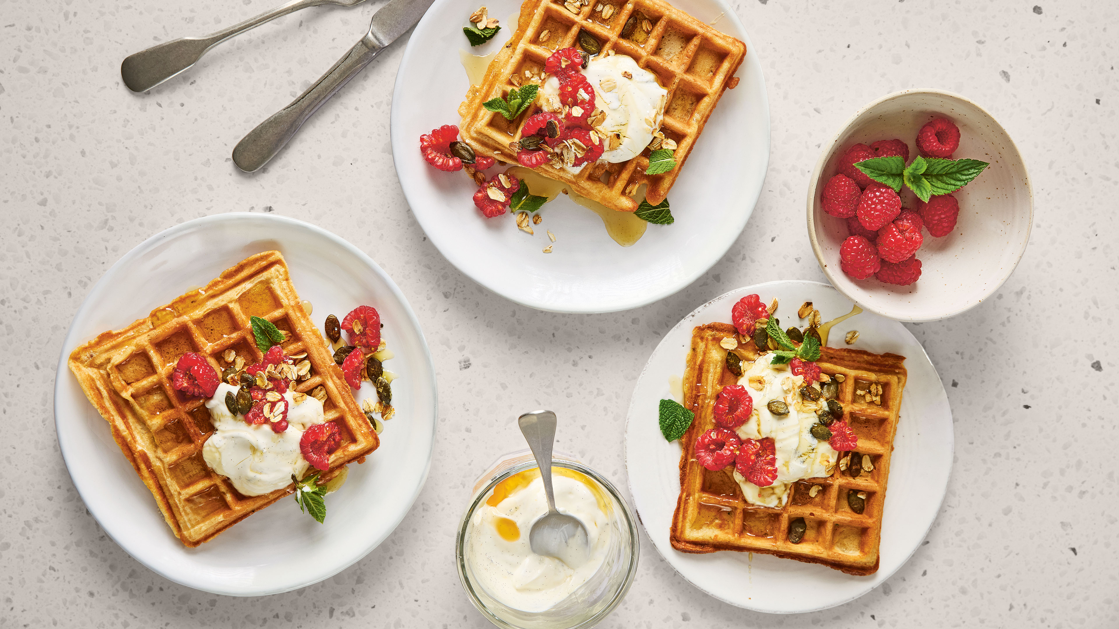Drei Teller mit jeweils einer Waffel, etwas heller Creme und Himbeeren