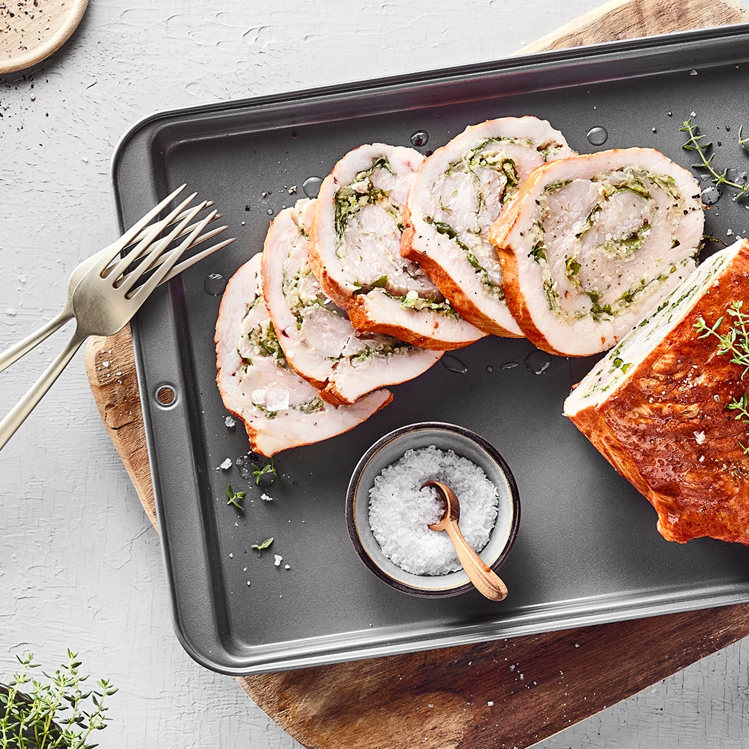 Auf einem Blech liegen Scheiben eines gefüllten Bratens mit Thymian, daneben Salzschale und Gabeln.