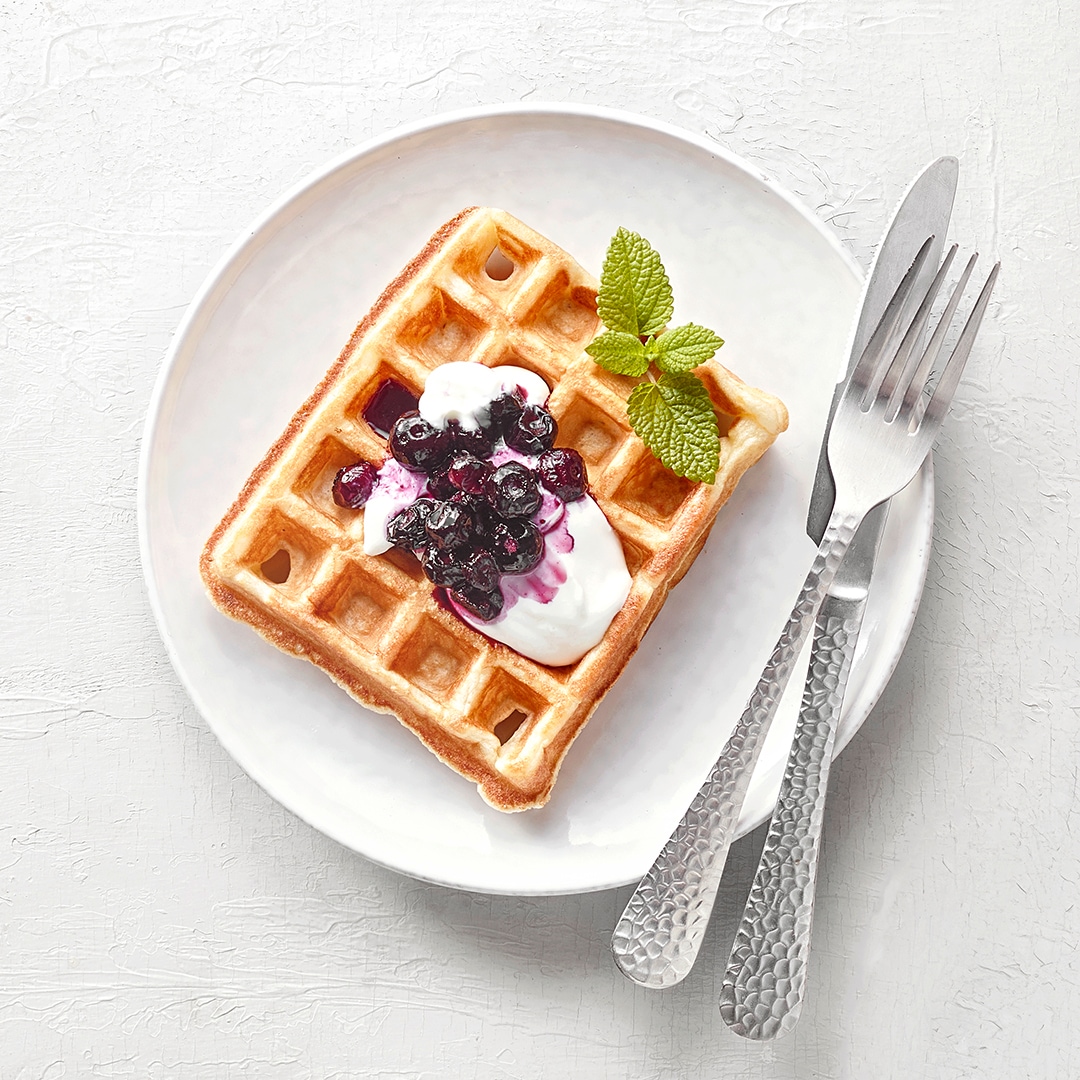 Teller mit quadratischer Waffel mit heller Creme und Beerenkompott.