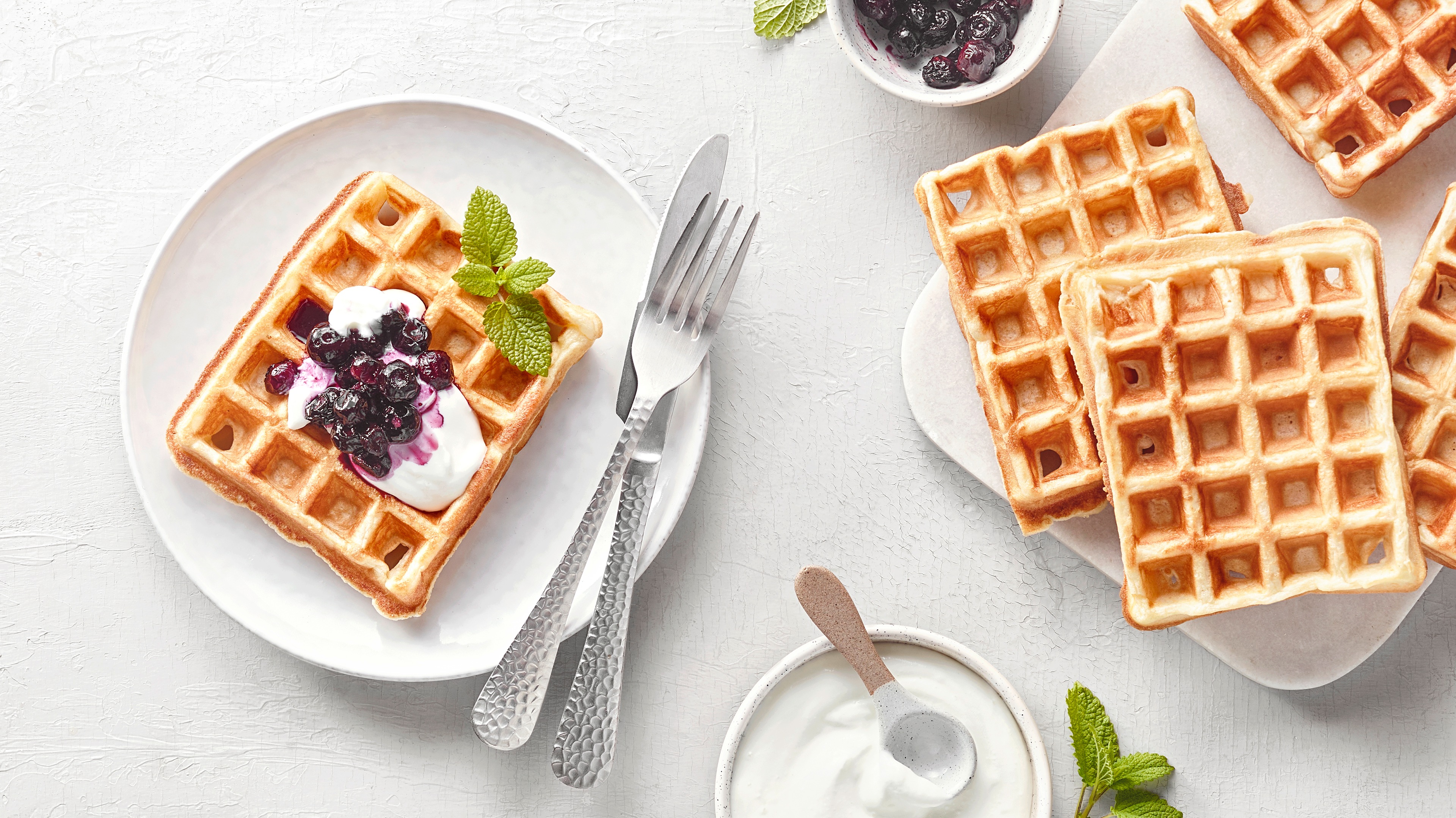 Teller mit quadratischer Waffel mit heller Creme und Beerenkompott. Daneben weitere Waffeln.
