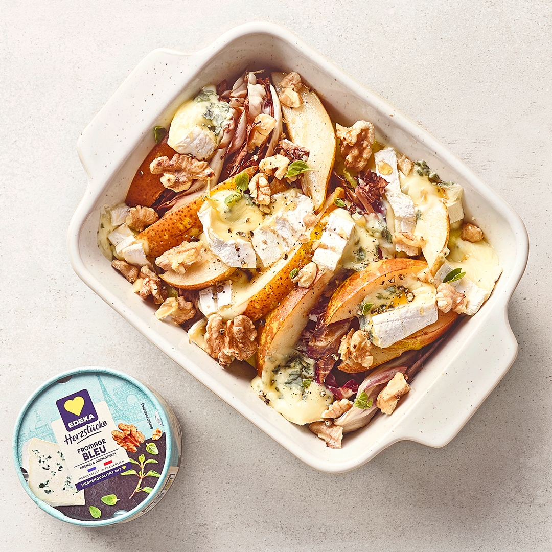 Überbackener Radicchio mit Birnenspalten, Camembert und Walnüssen in einer Auflaufform, daneben EDEKA Herzstücke Fromage Bleu.