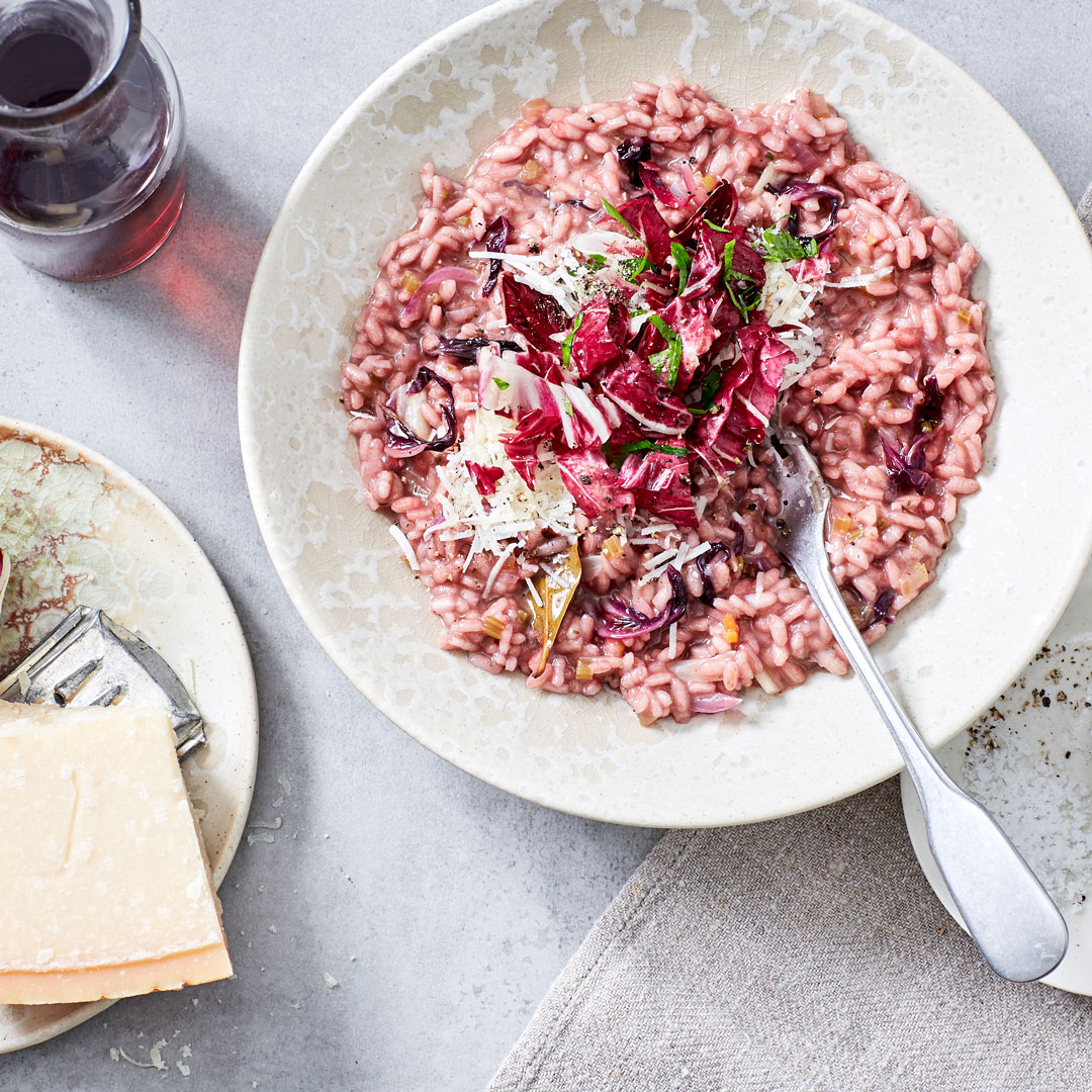 Teller mit rötlichem cremigen Risotto und Radicchioblättern, daneben Parmesan