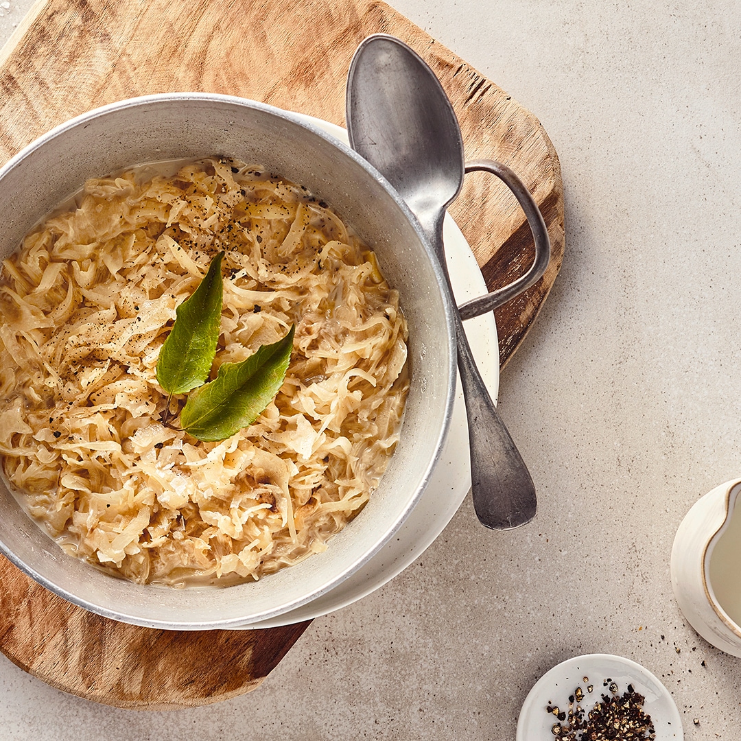 Ein gusseiserner Topf mit Sauerkraut in cremiger heller Soße, getoppt mit zwei Lorbeerblättern