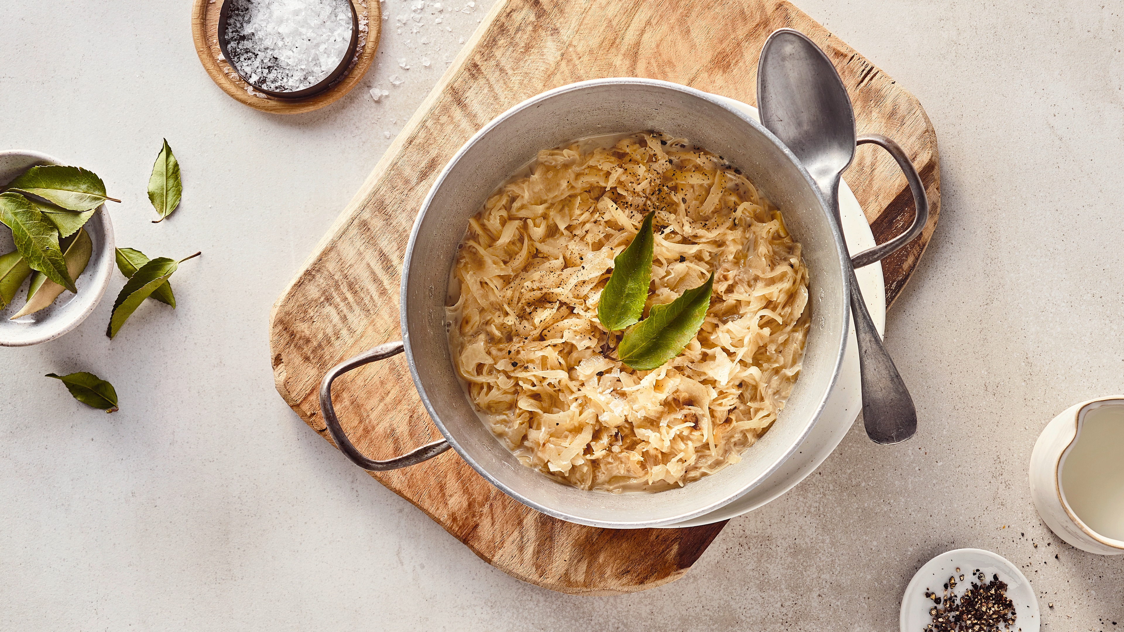 Rezept für Rahmsauerkraut Ein gusseiserner Topf mit Sauerkraut in cremiger heller Soße, getoppt mit zwei Lorbeerblättern