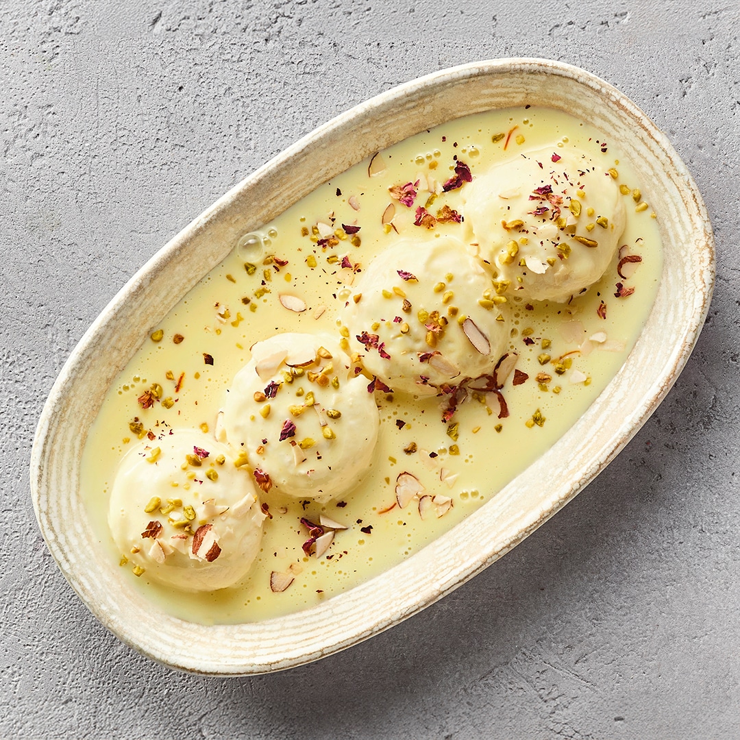 Ein Teller mit weißen Bällchen in gelber Soße, bestreut mit Pistazienstücken und dünnen Mandelblättchen.
