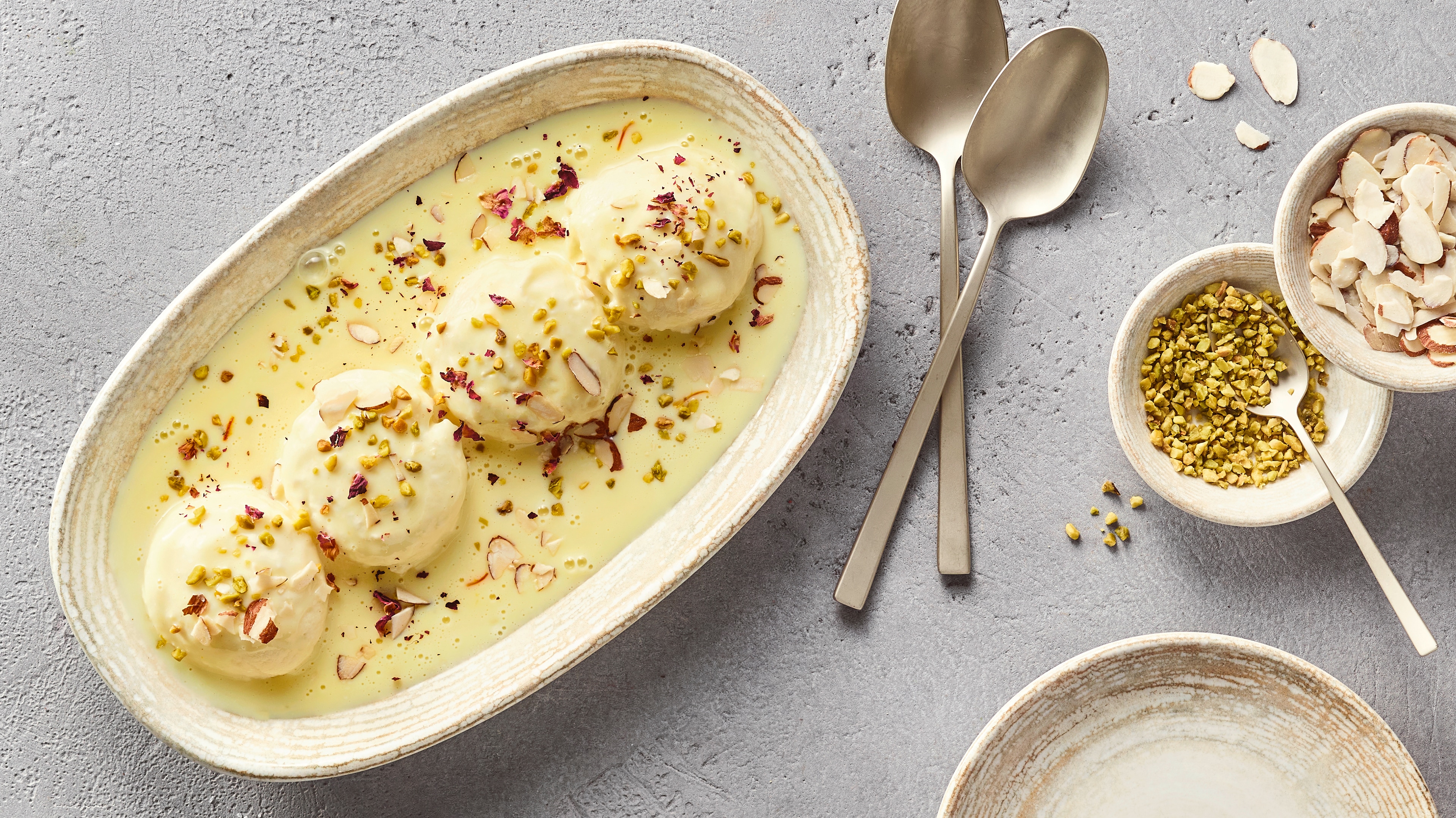 Ein Teller mit weißen Bällchen in gelber Soße, bestreut mit Pistazienstücken und dünnen Mandelblättchen.