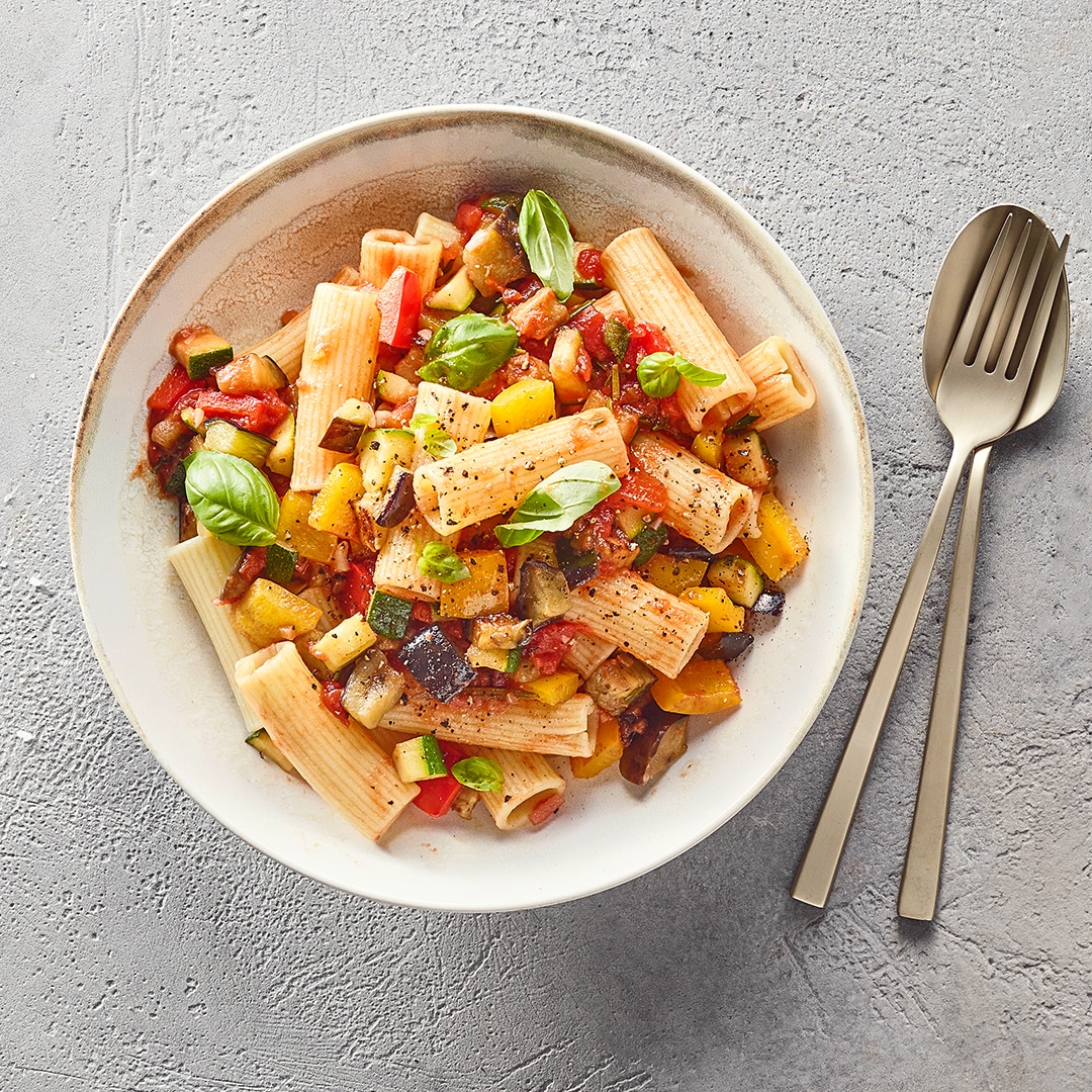 Nudeln mit bunten Gemüsestücken und Basilikumblättern auf großem tiefen Teller