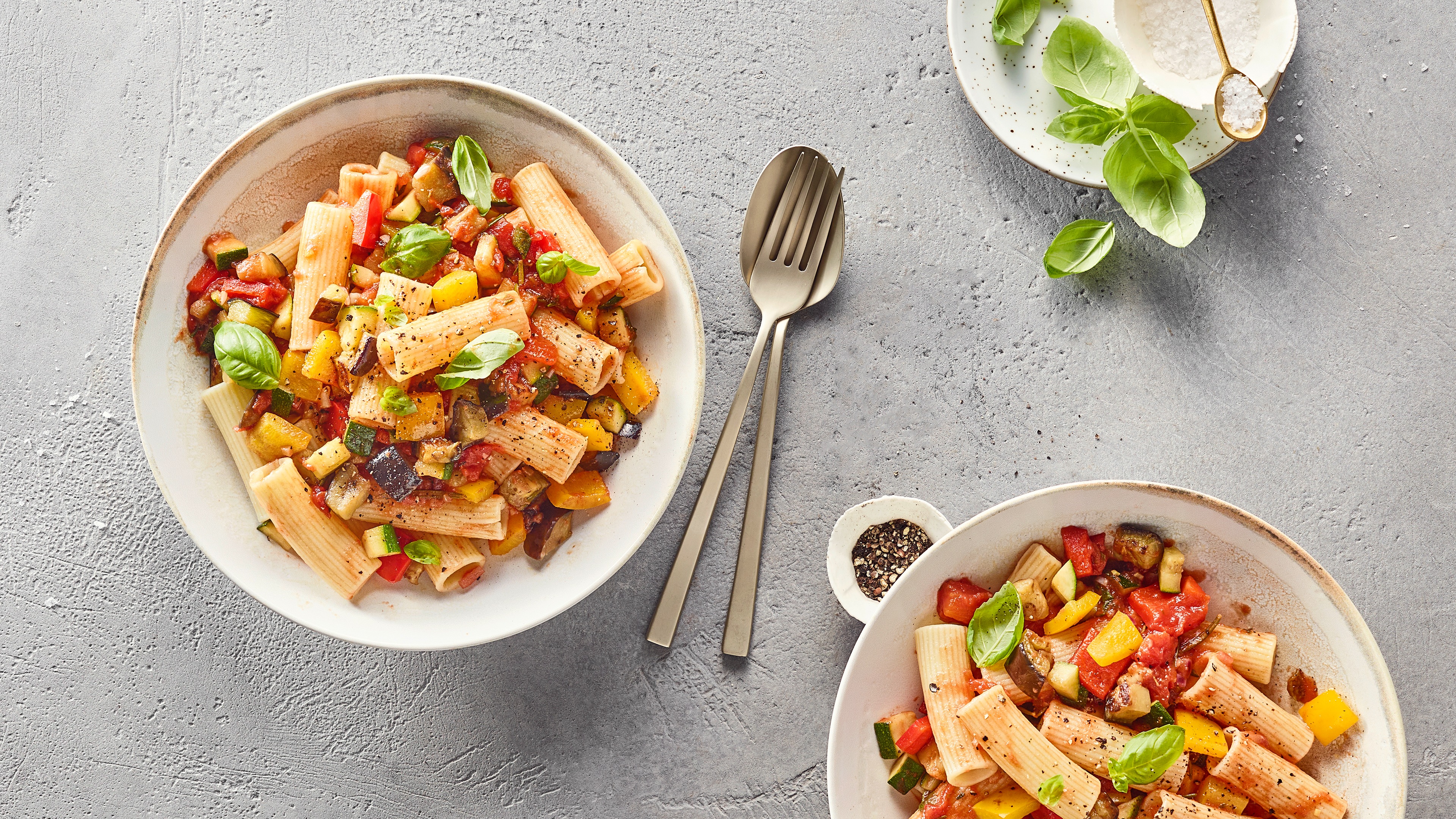 Nudeln mit bunten Gemüsestücken und Basilikumblättern auf großem tiefen Teller