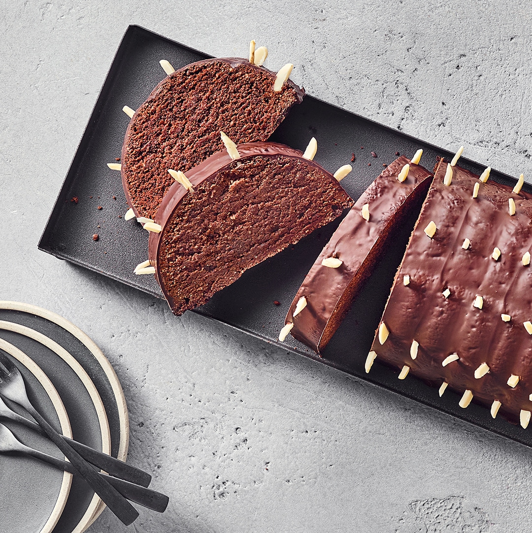 Ein Teller mit dunklem Schokokuchen, überzogen mit glänzendem Guss und bestreut mit hellen Mandelstiften, in Scheiben geschnitten.