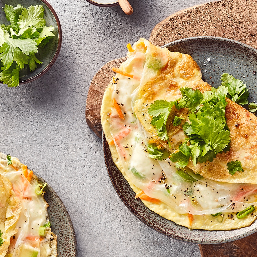 Gefüllte Omeletts mit Reispapier, Gemüse und frischem Koriander auf Keramiktellern.