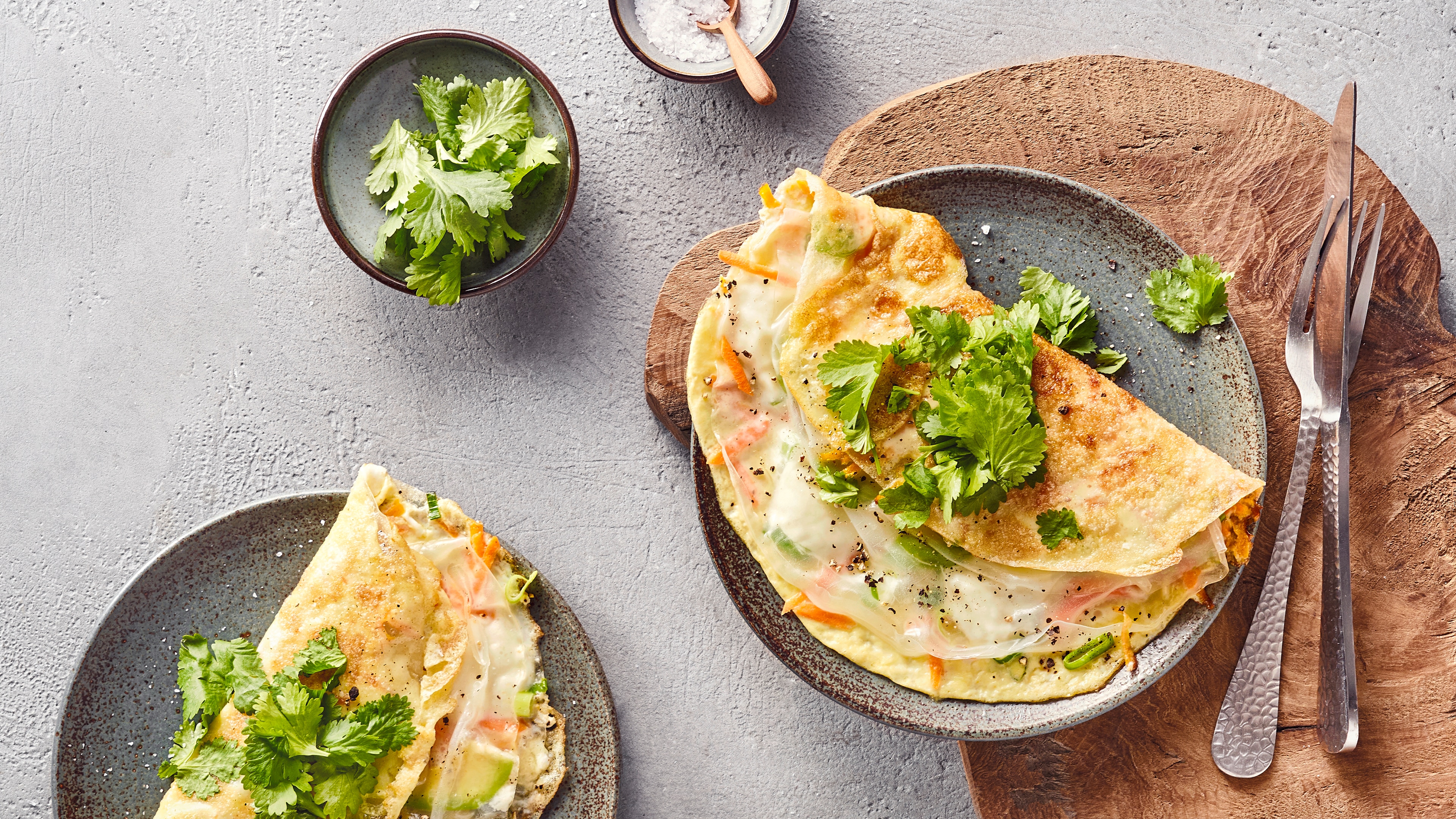 Gefüllte Omeletts mit Reispapier, Gemüse und frischem Koriander auf Keramiktellern.