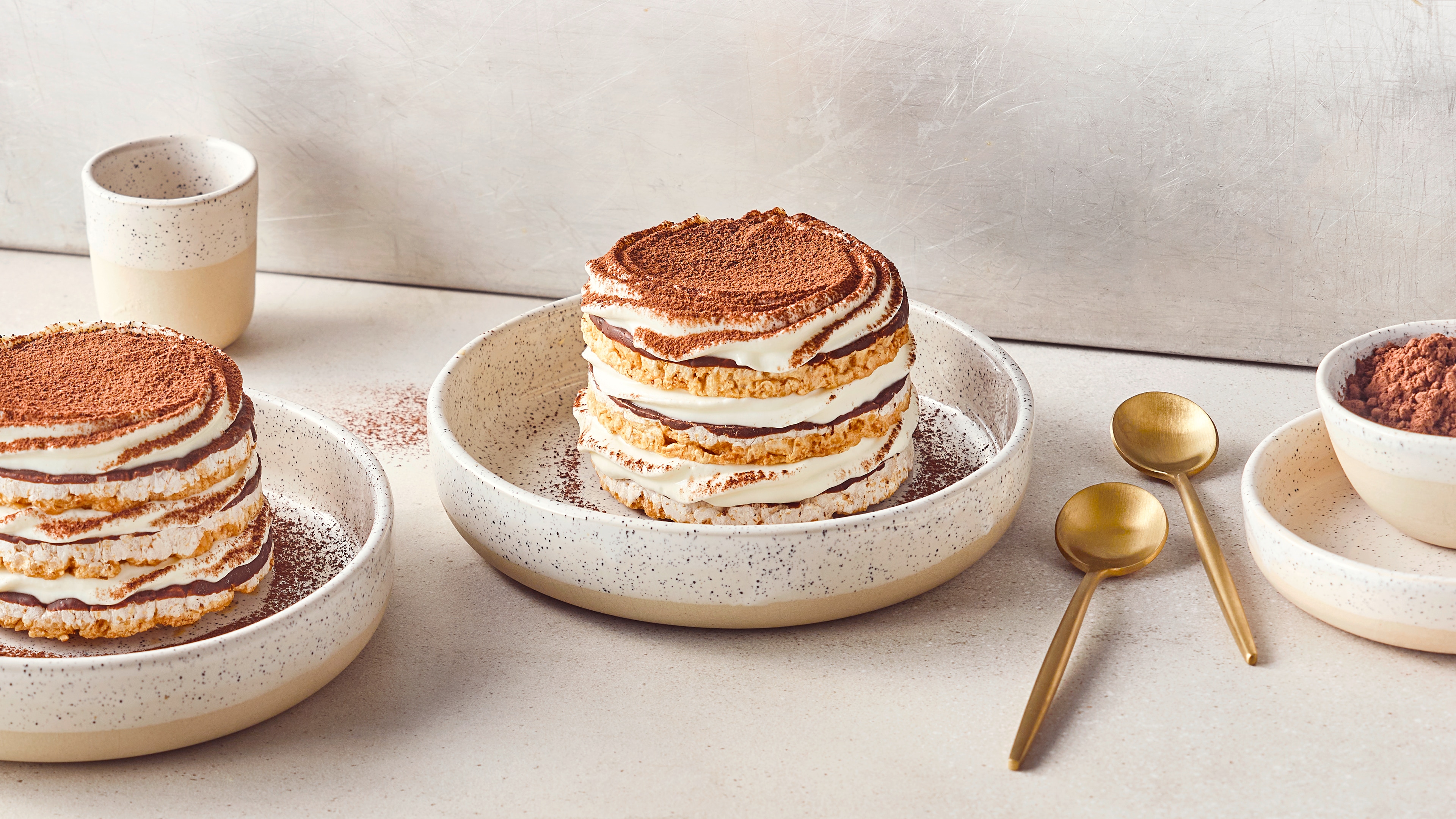 Ein Turm, geschichtet aus Reiswaffeln, heller Creme und Kakaopulver, auf einem rustikalen Teller