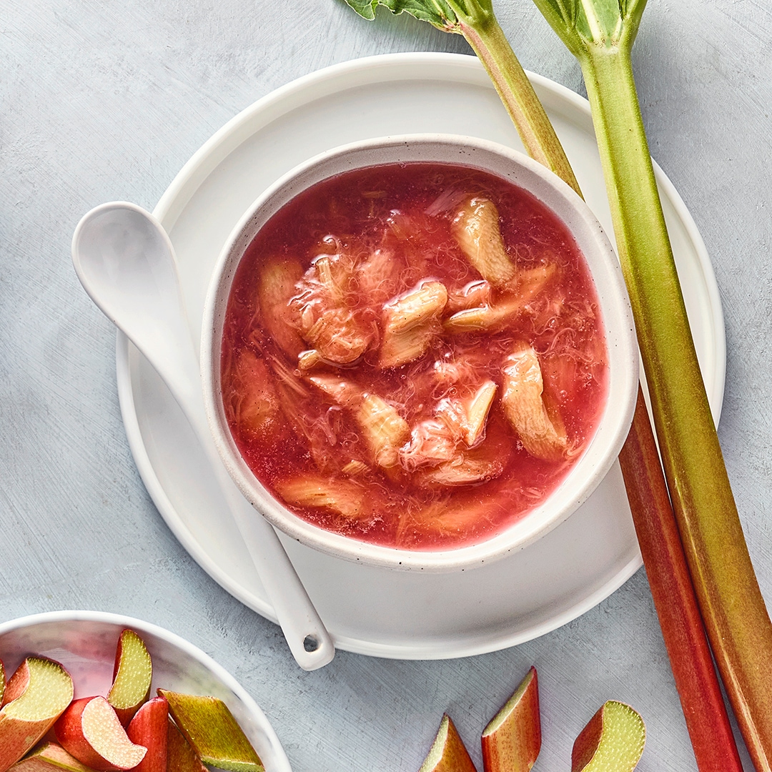 Rötlicher Kompott in Schale, daneben Rhabarberstangen und Stücke