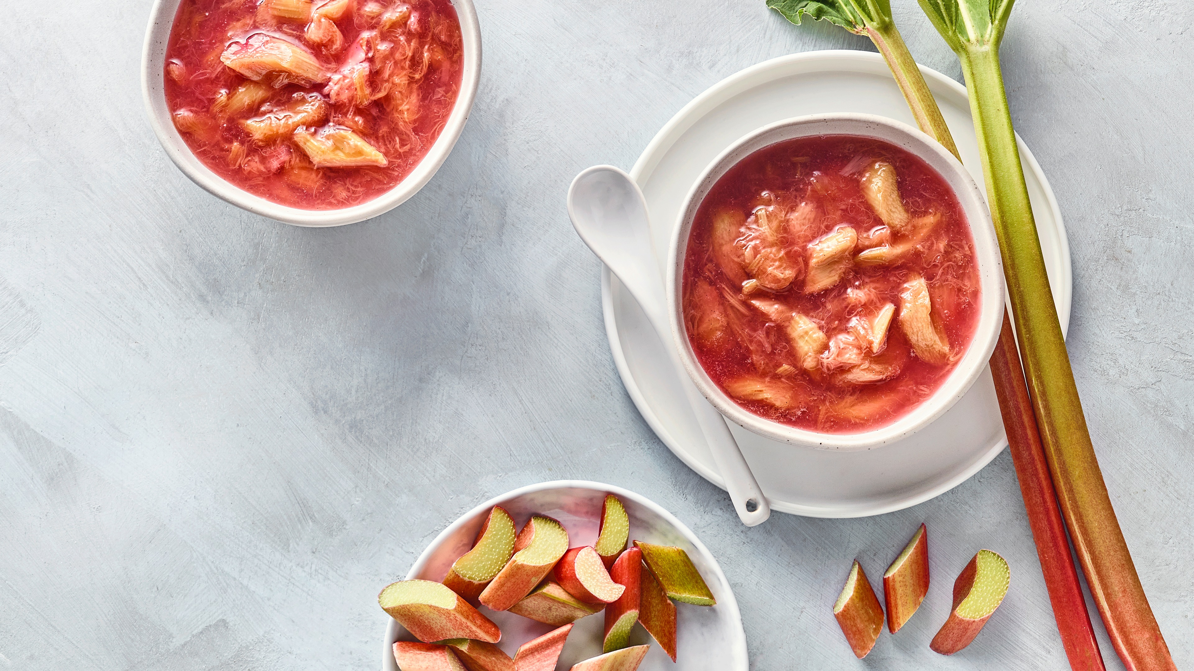 Rötlicher Kompott in zwei Schalen, daneben Rhabarberstangen und Stücke