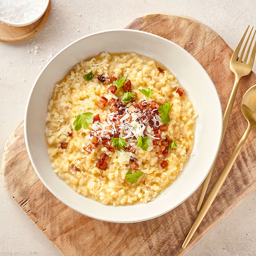 Eine Schale mit cremigem Risotto-Reis, garniert mit Schinkenwürfeln, geriebenem Käse und frischer Petersilie