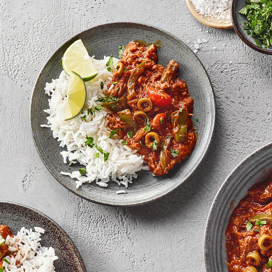Teller mit weißem Reis und rötlichem Ragout mit Oliven. Daneben großer Teller mit Ragout.