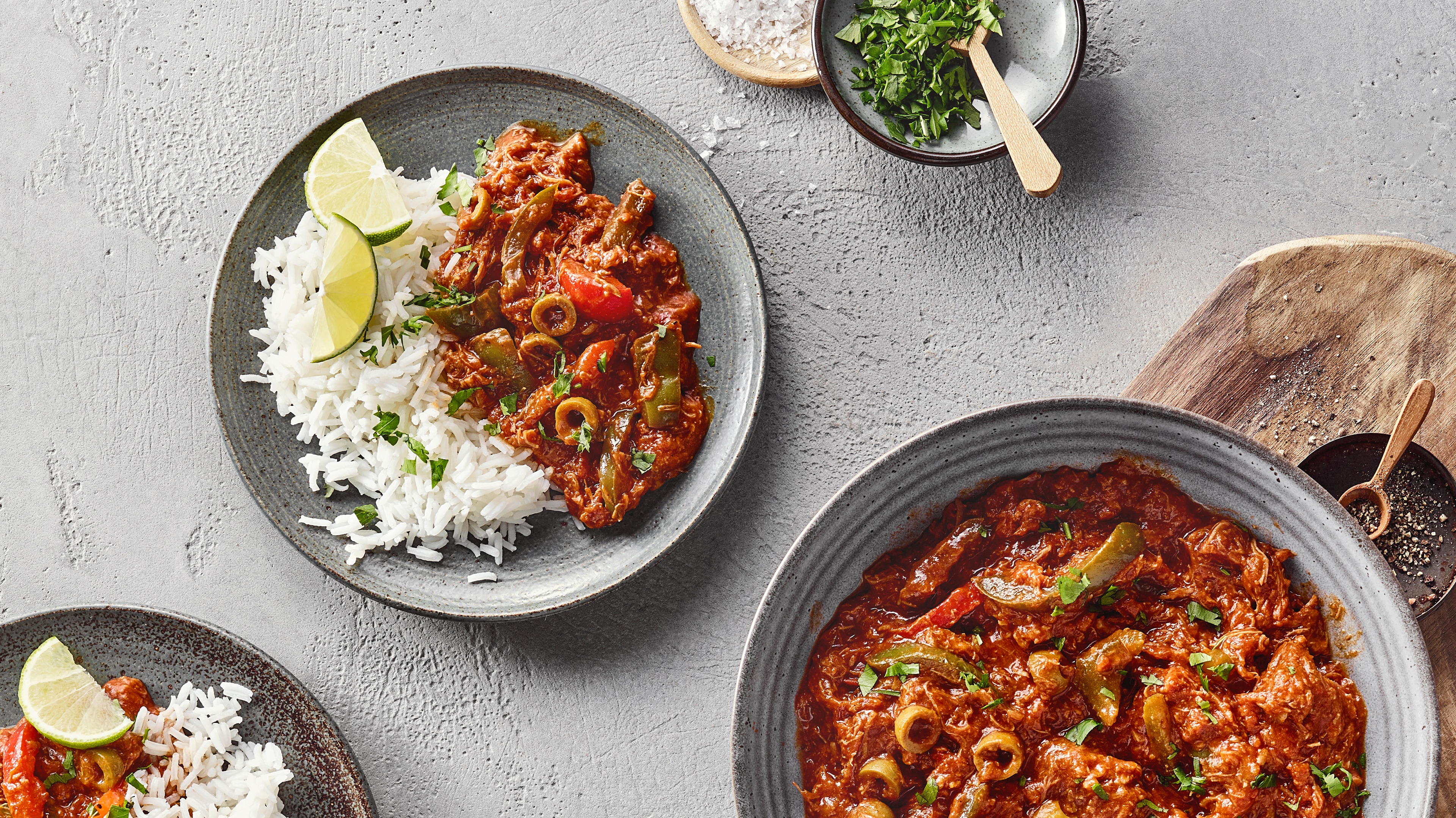 Teller mit weißem Reis und rötlichem Ragout mit Oliven. Daneben großer Teller mit Ragout.