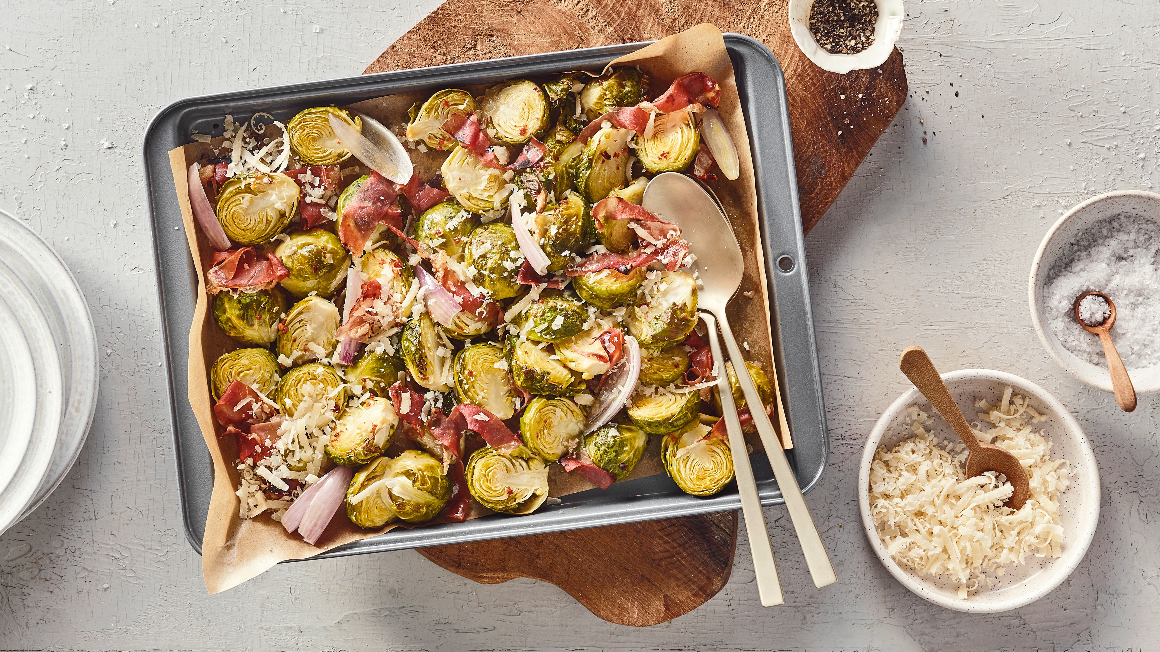 Ein Blech mit halbierten grünen Röschen, roten Streifen, weißen Flocken und länglichen Stücken auf braunem Papier.