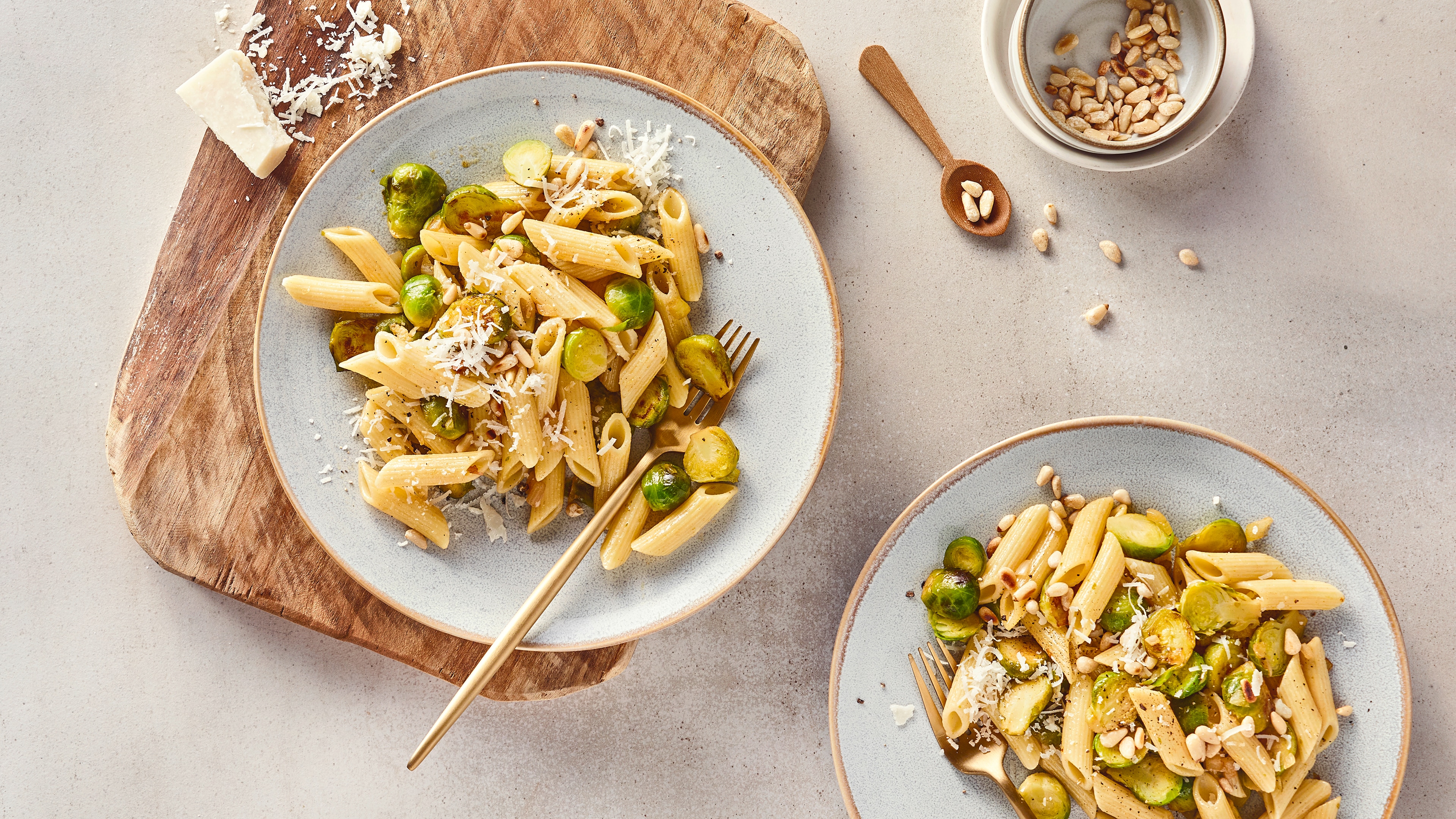 Runde Teller mit Penne-Pasta, getoppt mit geröstetem Rosenkohl, geriebenem Hartkäse und gerösteten Pinienkernen