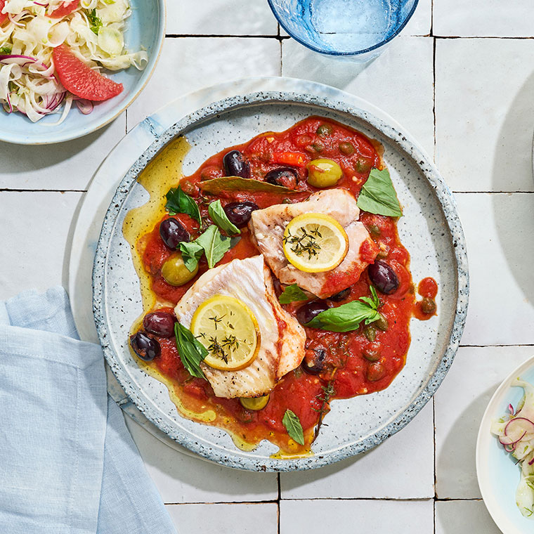 Teller mit roter Sauce, Oliven und mit Zitronen-garnierten Fischfilets.