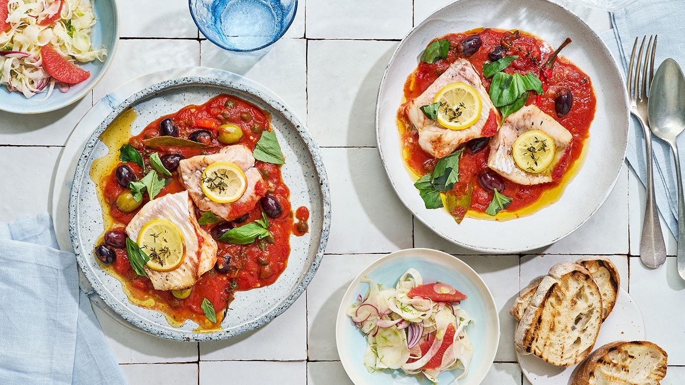 2 Teller mit roter Sauce, Oliven und mit Zitronen-garnierten Fischfilets