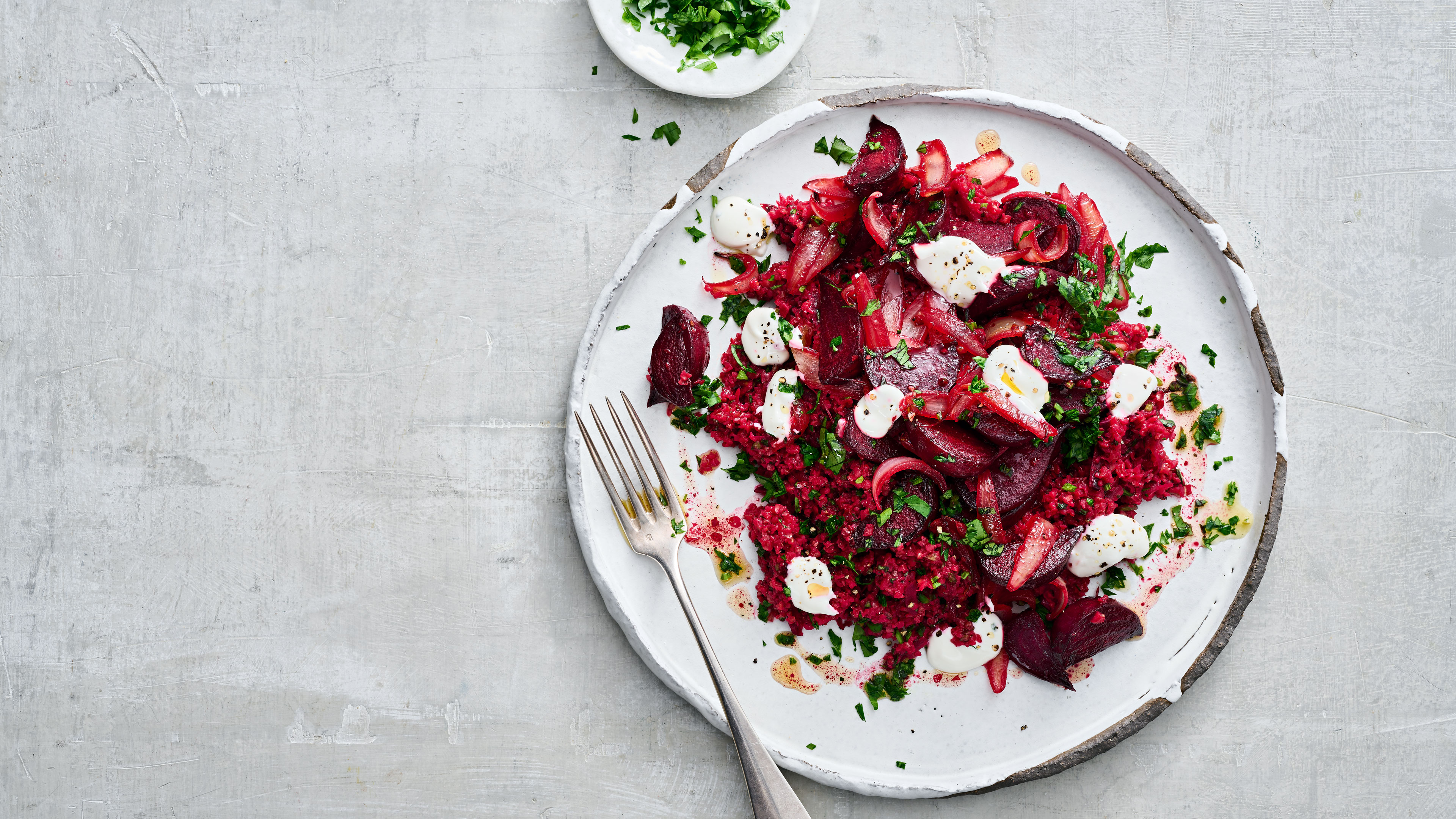 Roter Salat mit Roter Bete, Bulgur und kleinen Mozzarella-Kugeln auf einem weißen Teller, garniert mit frischen Kräutern.
