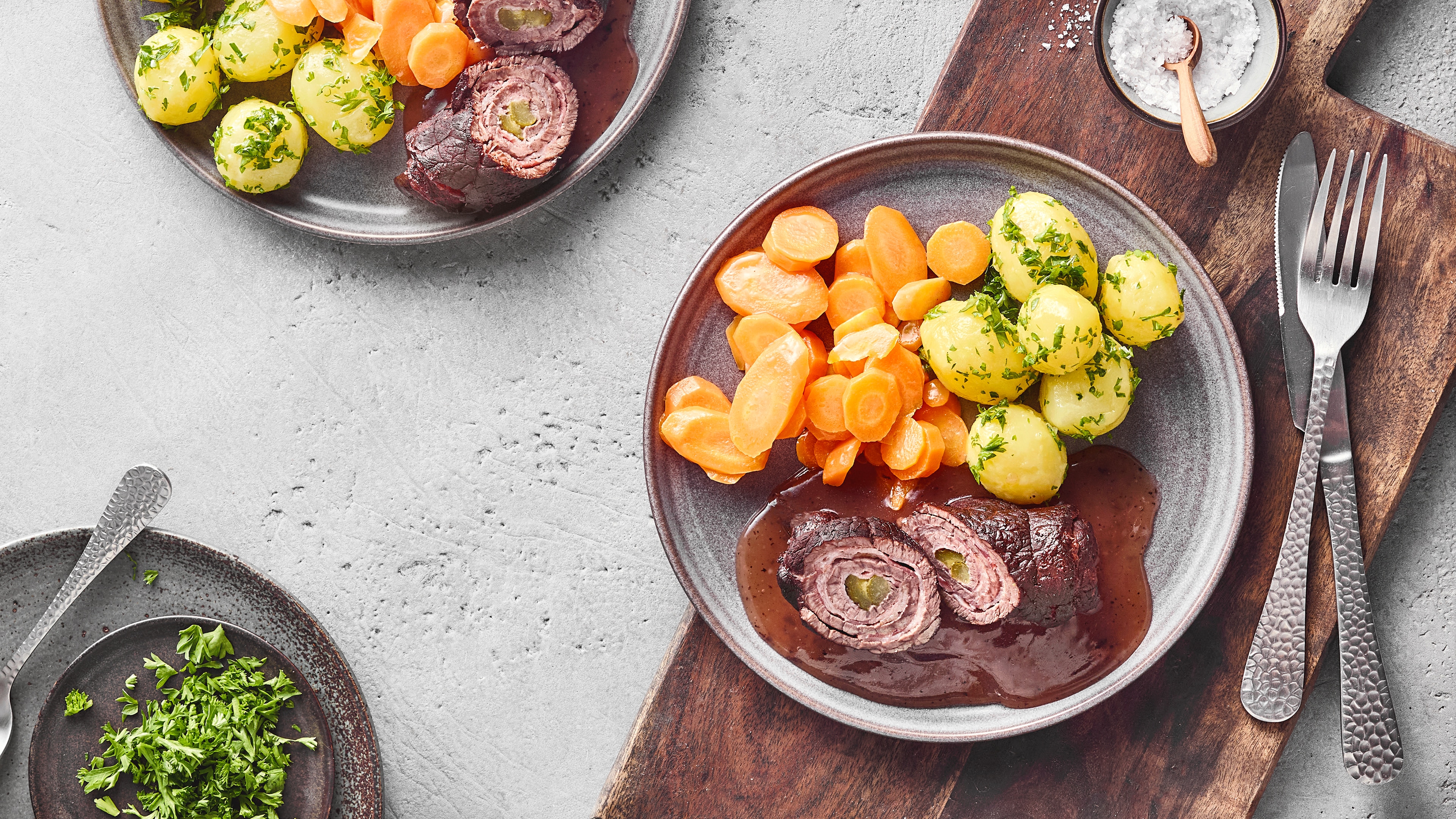Rinderroulade mit Soße, Petersilienkartoffeln und glasierten Möhren auf einem Teller.