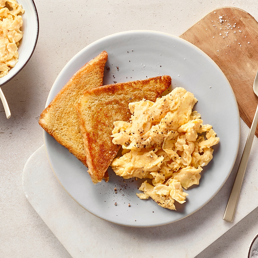 Ein Teller mit gelbem Rührei, bestreut mit Pfeffer, daneben zwei goldbraune Toastscheiben.