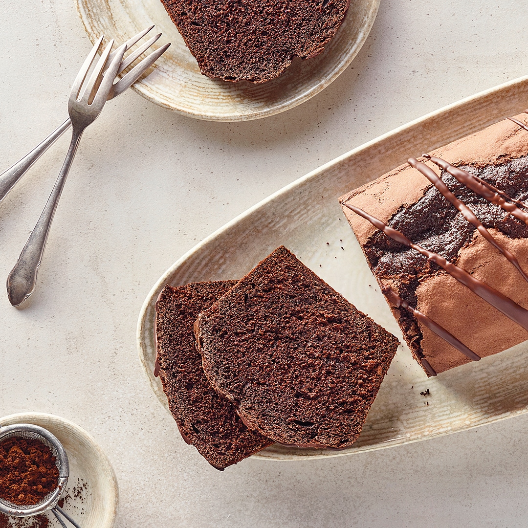 Ein ovaler Teller mit dunkelbraunen, saftigen Kastenkuchen, davor liegen zwei abgeschnittene Kuchenstücke, darüber Schokoglasur