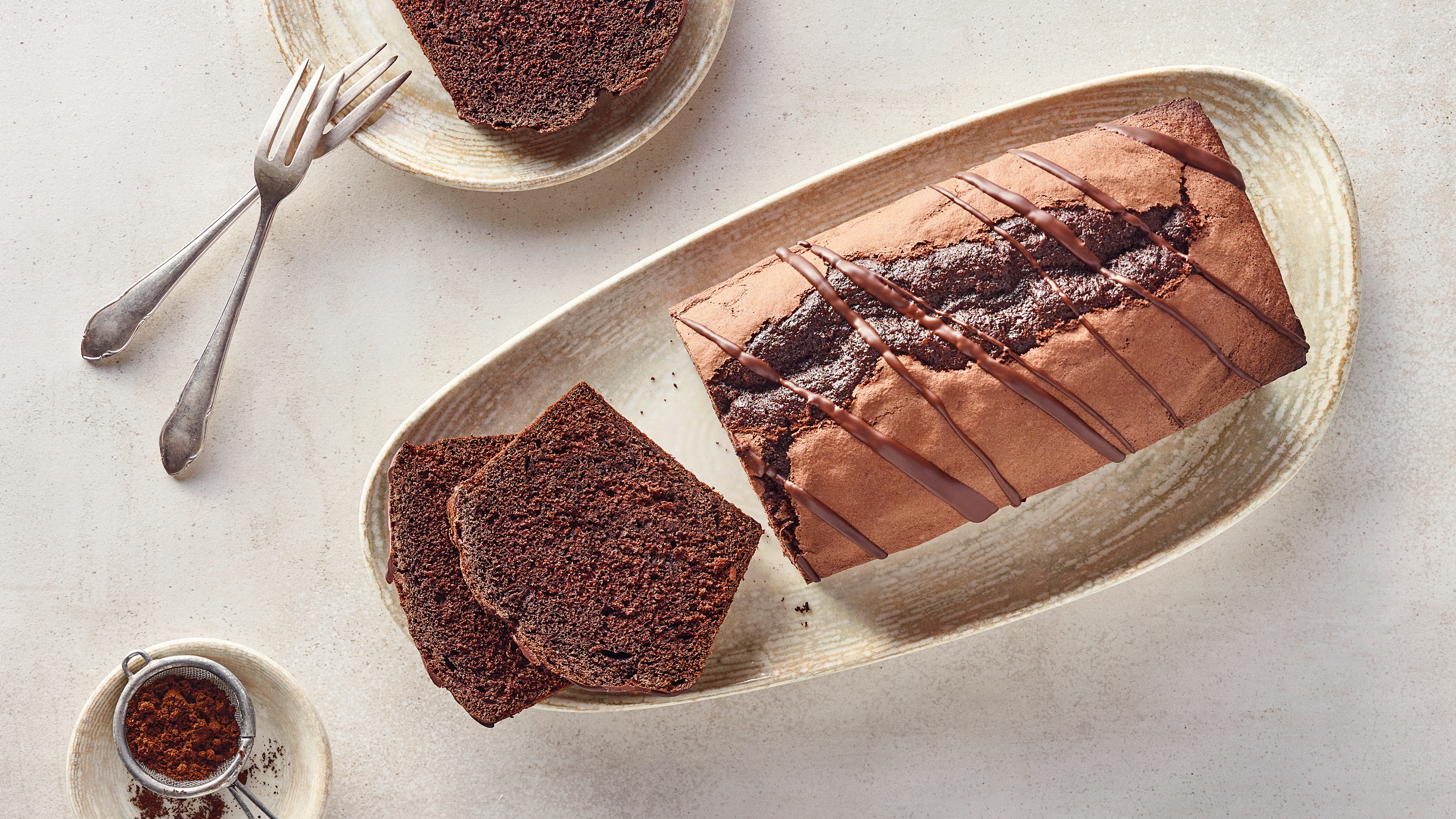 Ein ovaler Teller mit dunkelbraunen, saftigen Kastenkuchen, davor liegen zwei abgeschnittene Kuchenstücke, darüber Schokoglasur