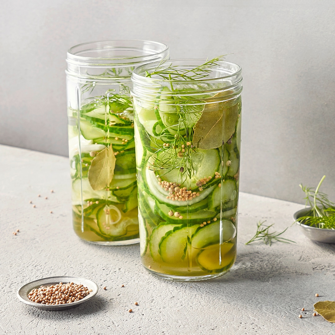 Dünne Gurkenscheiben mit Kräutern und Flüssigkeit in Gläsern