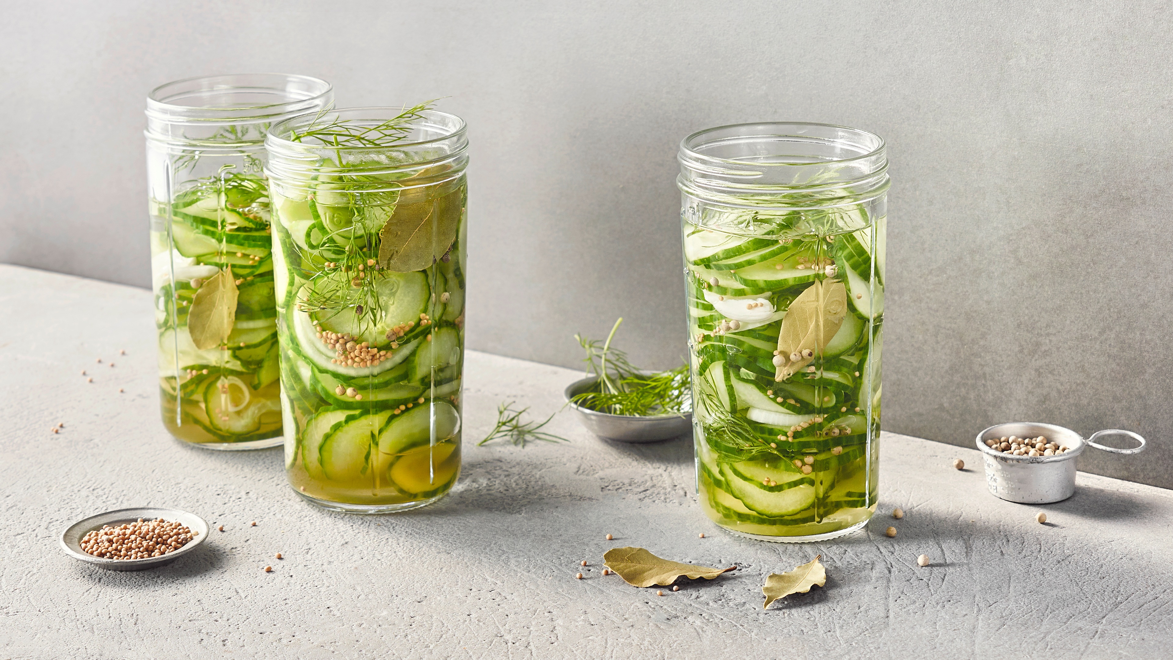 Dünne Gurkenscheiben mit Kräutern und Flüssigkeit in Gläsern