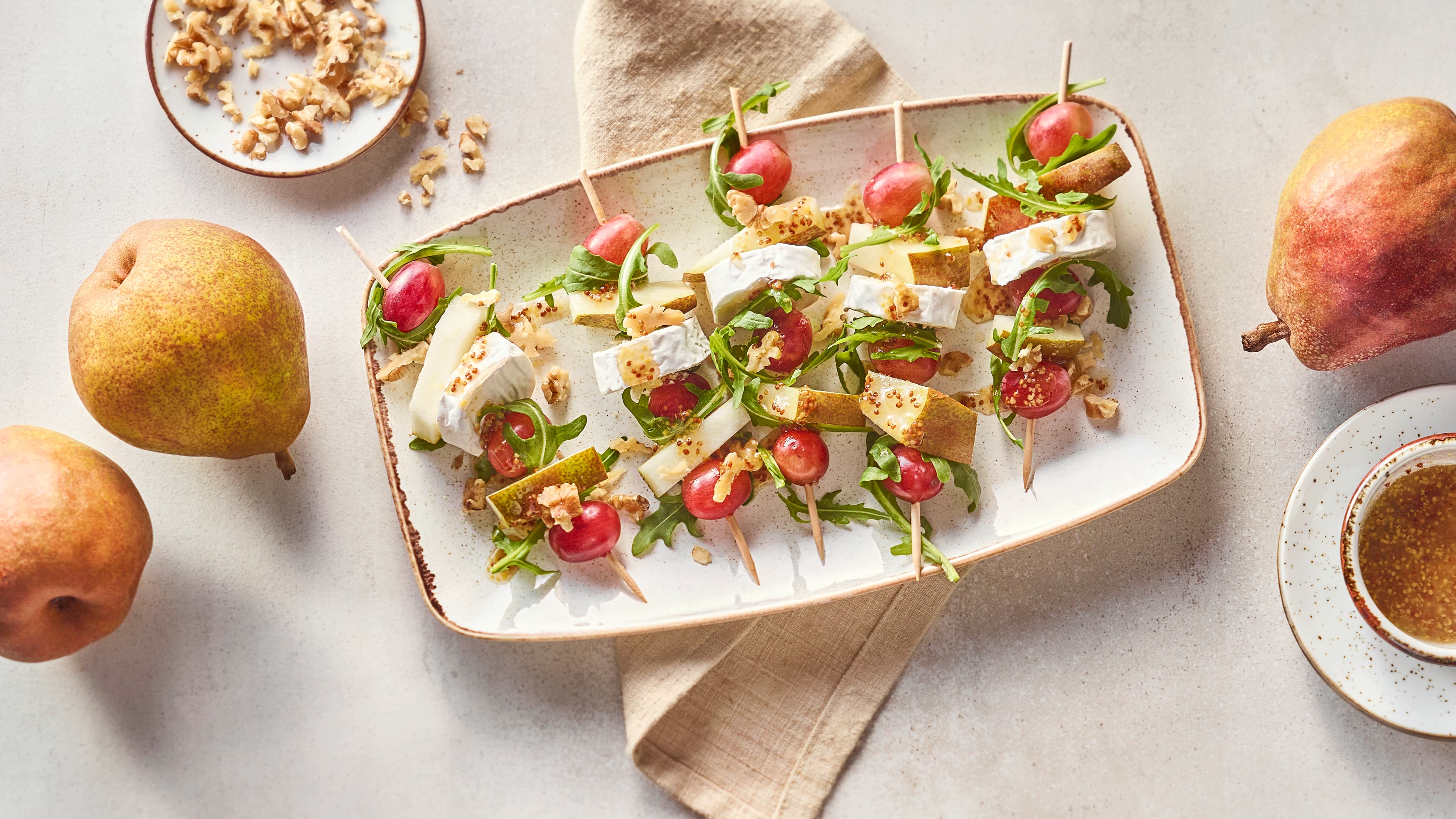 Rezept für Salatspieße mit Birne Holzspieße mit Rucola, Birne, Weintrauben und Ziegenkäse auf Teller