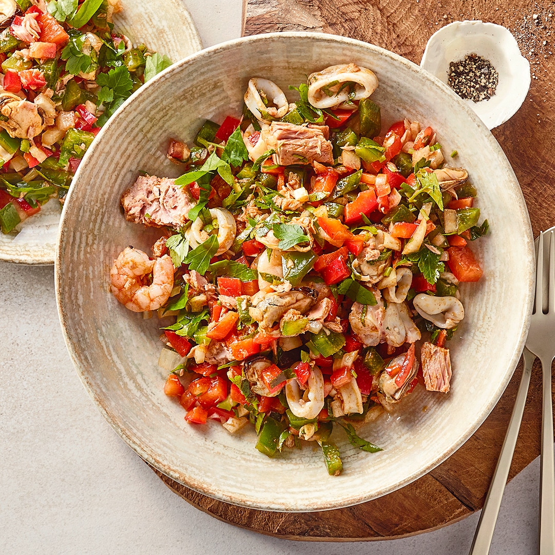 Eine Schüssel mit gemischtem Salat aus grünen Blättern, roten Paprikastücken, Meeresfrüchten und Thunfischstücken.