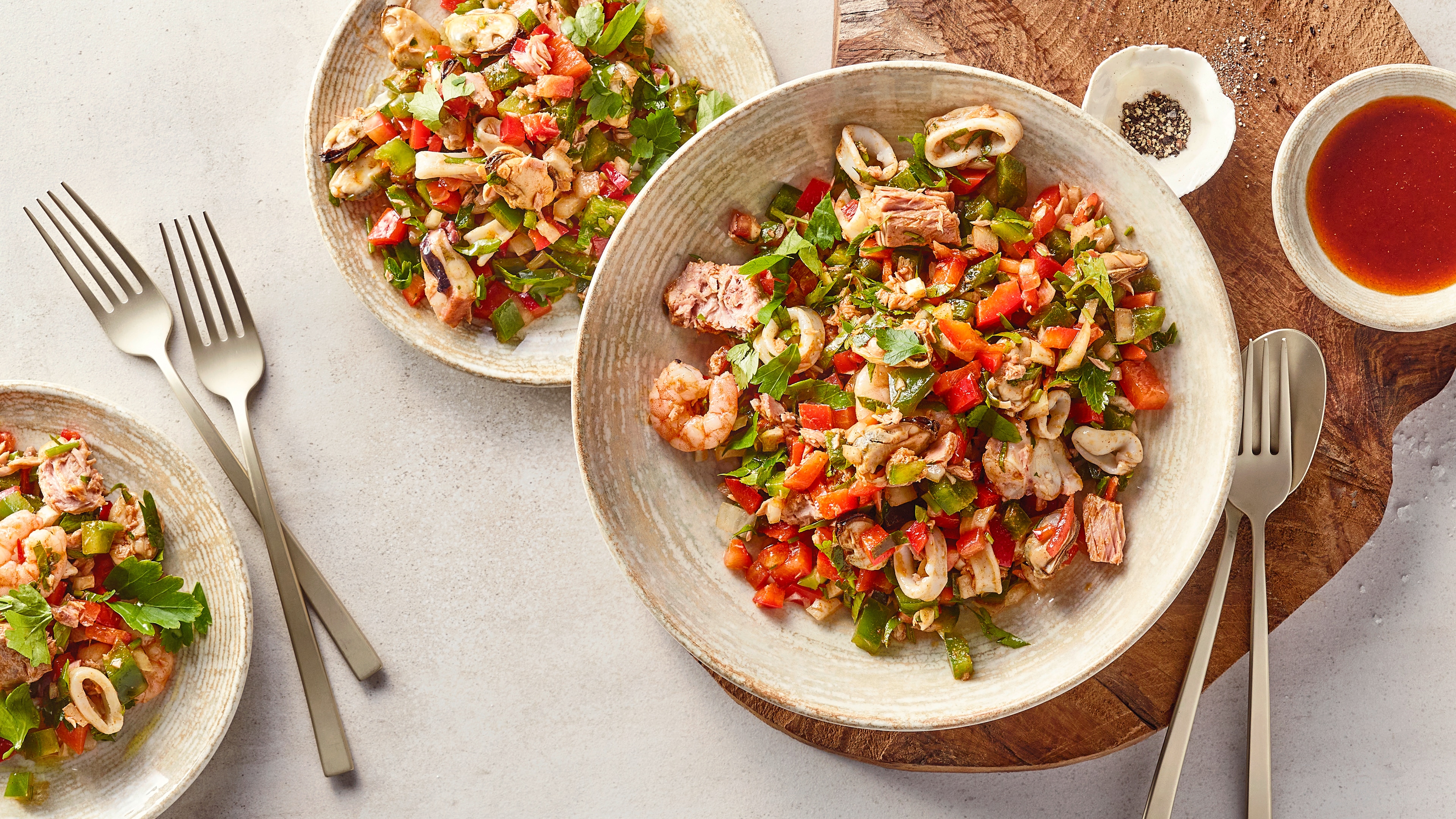 Eine Schüssel mit gemischtem Salat aus grünen Blättern, roten Paprikastücken, Meeresfrüchten und Thunfischstücken.