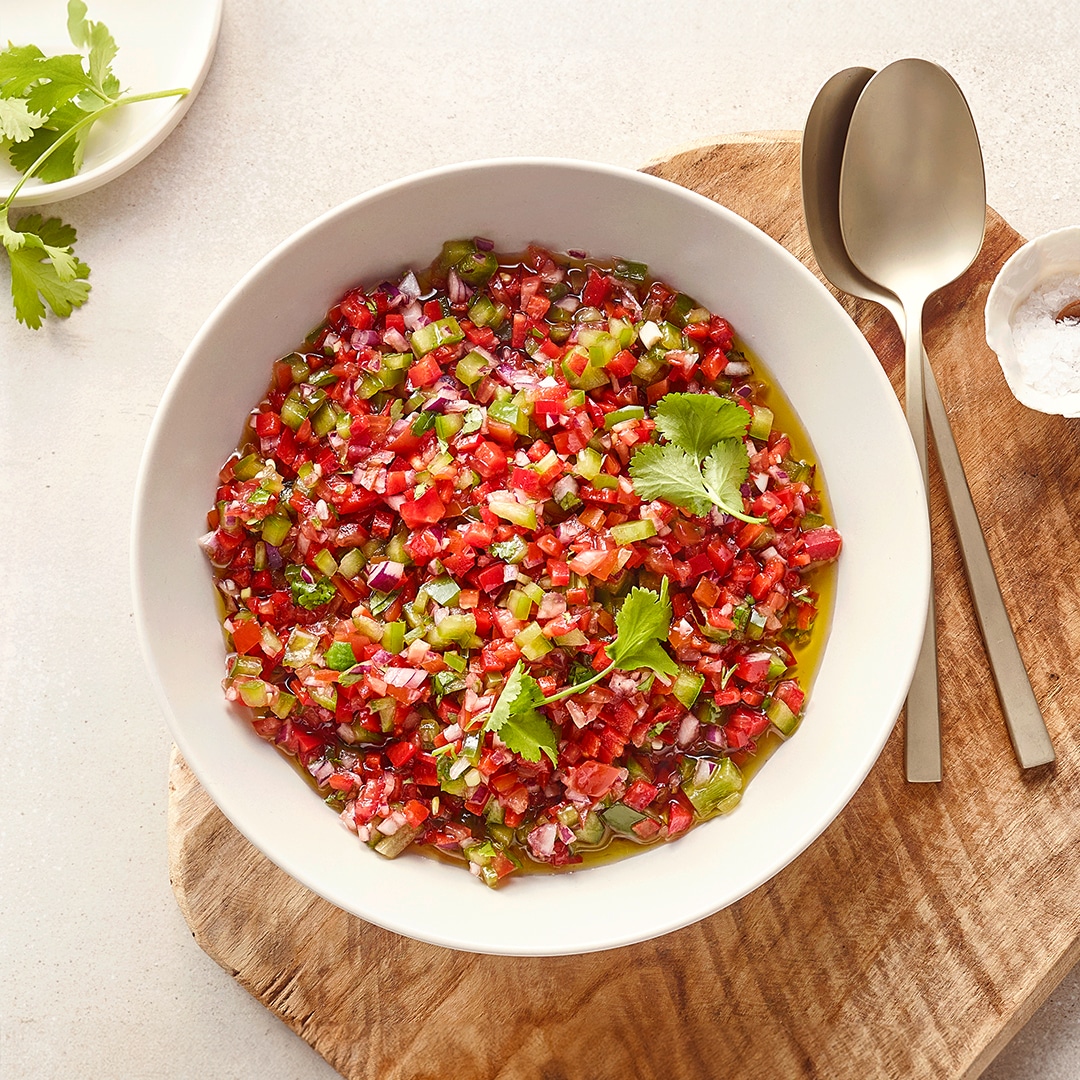 Große Schale mit kleinen roten, grünen und lilanen Stücken in Öl, daneben Koriander