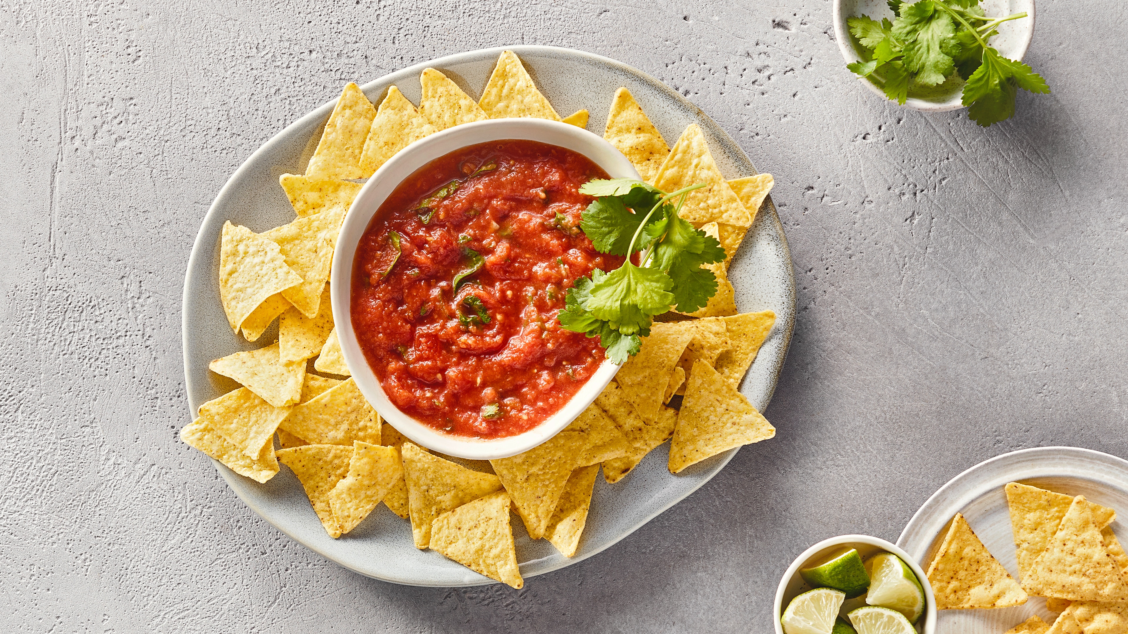 Ein Teller mit gelben Dreiecks-Chips und einer Schale roter Soße mit grünen Kräutern in der Mitte.