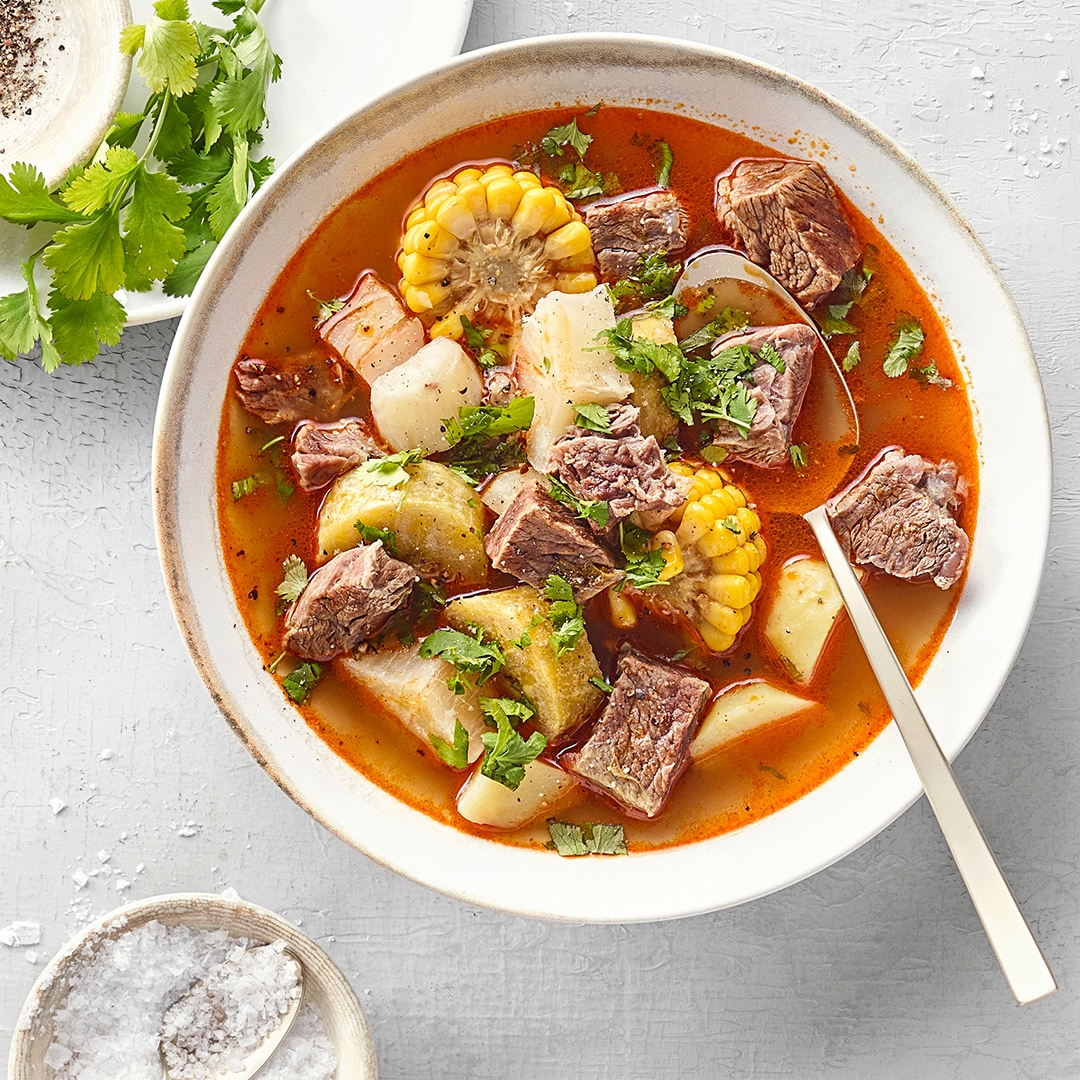 Brühiger Eintopf aus Fleisch, Wurzelgemüse, Maisscheiben und Koriander.