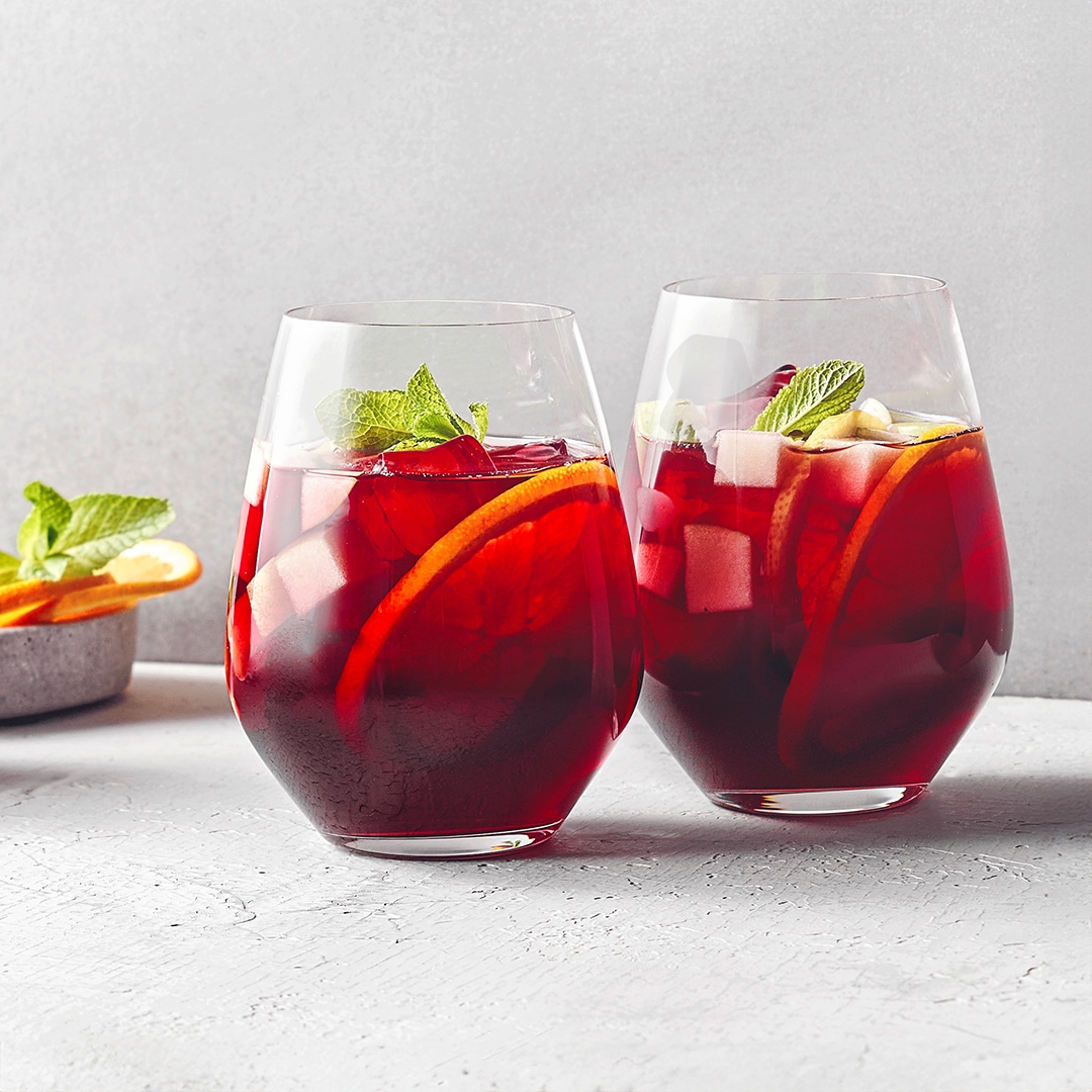 Zwei Gläser mit rotem Weinpunsch, Zitronenscheiben, Minzblättern und Eiswürfeln.