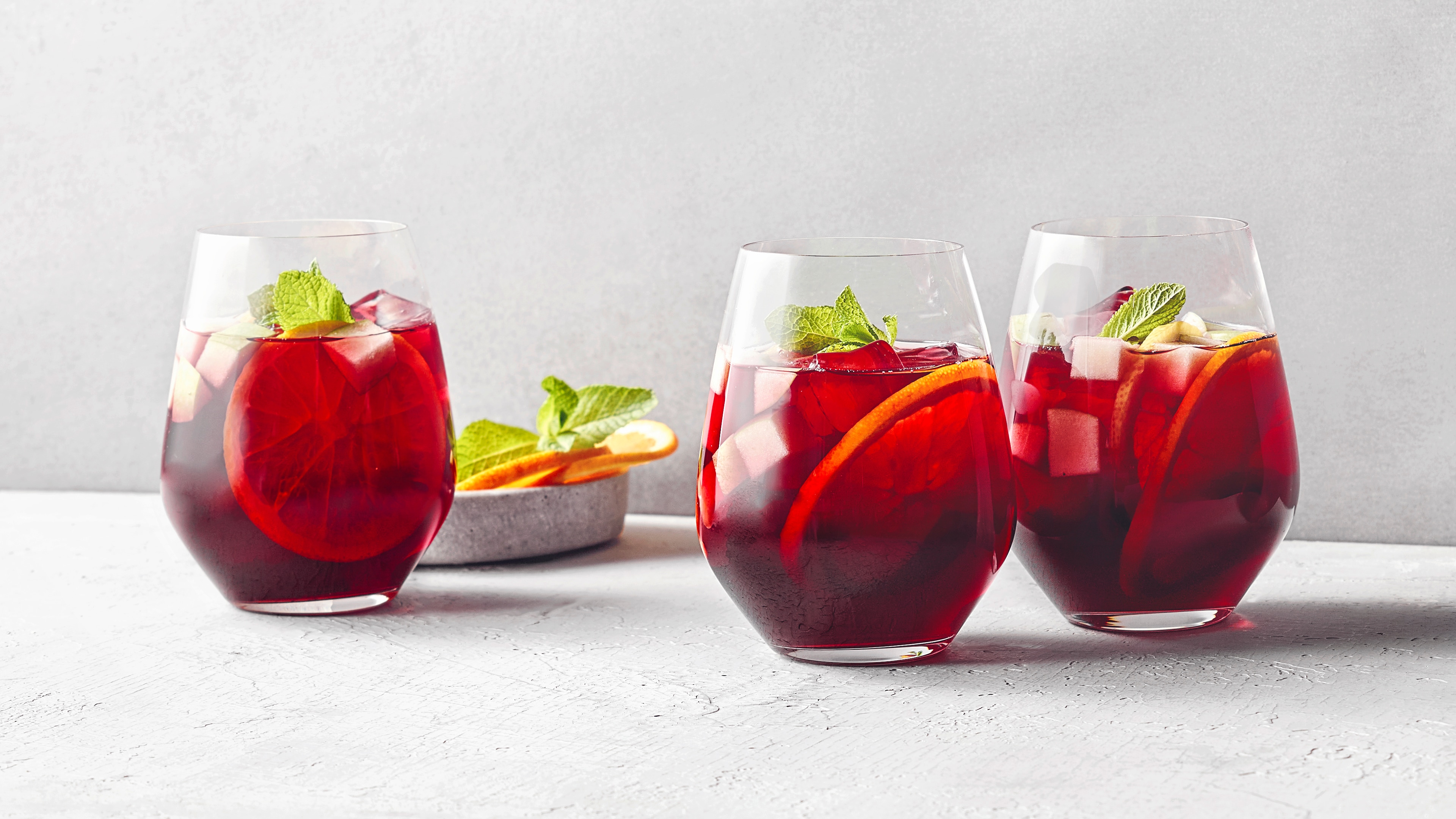 Drei Gläser mit rotem Weinpunsch, Zitronenscheiben, Minzblättern und Eiswürfeln.