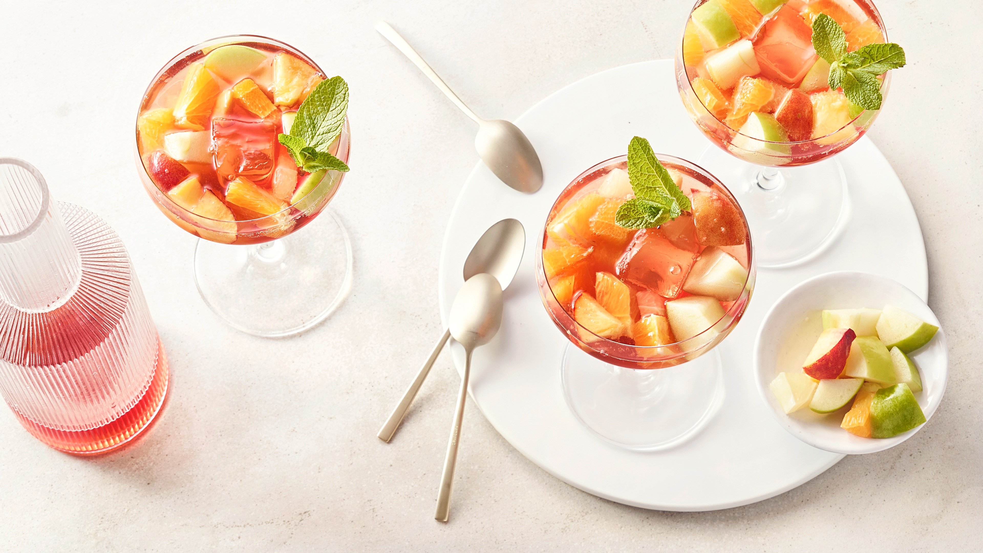 Draufsicht auf Gläser mit hellroter Flüssigkeit, Orangen- und Apfelstücken und Eiswürfeln.