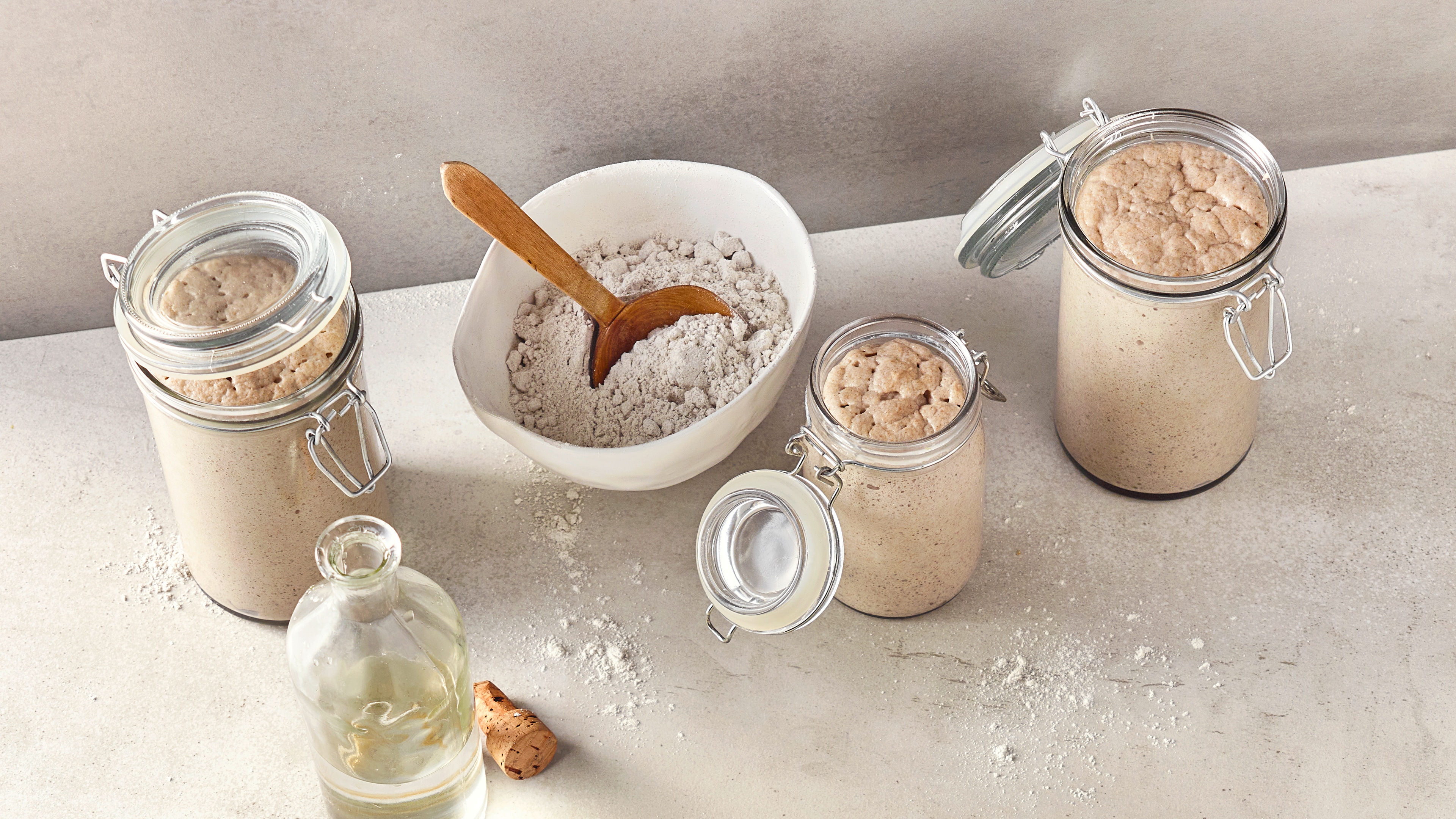 Rezept zum Ansetzen von Sauerteig Einmachgläser mit einem luftigen, hellen, homogenen Teig, daneben eine Schüssel mit feinem Mehl