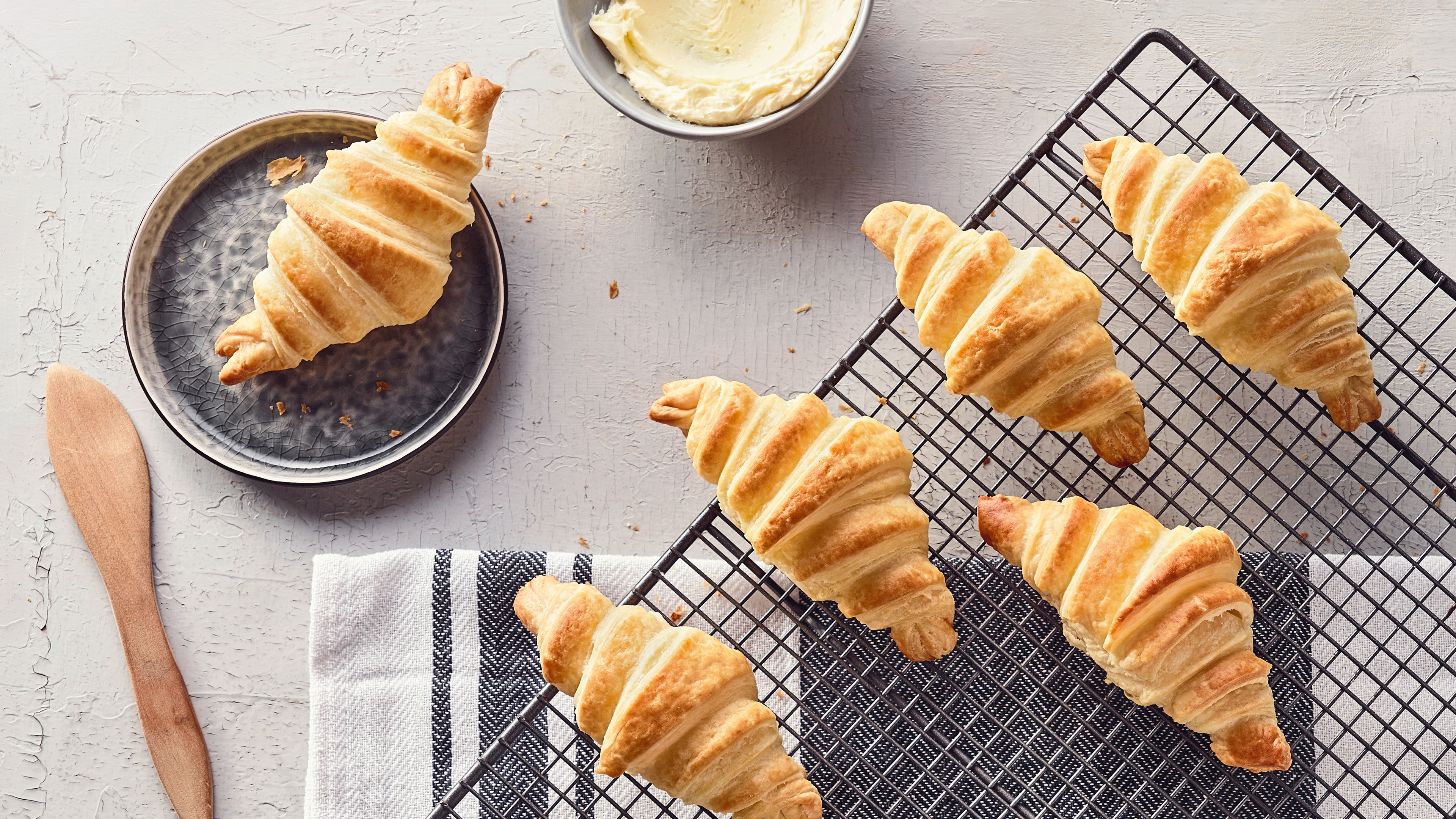 Rezept für Sauerteig-Croissants Knusprige, goldgelb gebackene Croissants auf einem Abkühlgitter, daneben ein Schälchen mit luftiger Butter