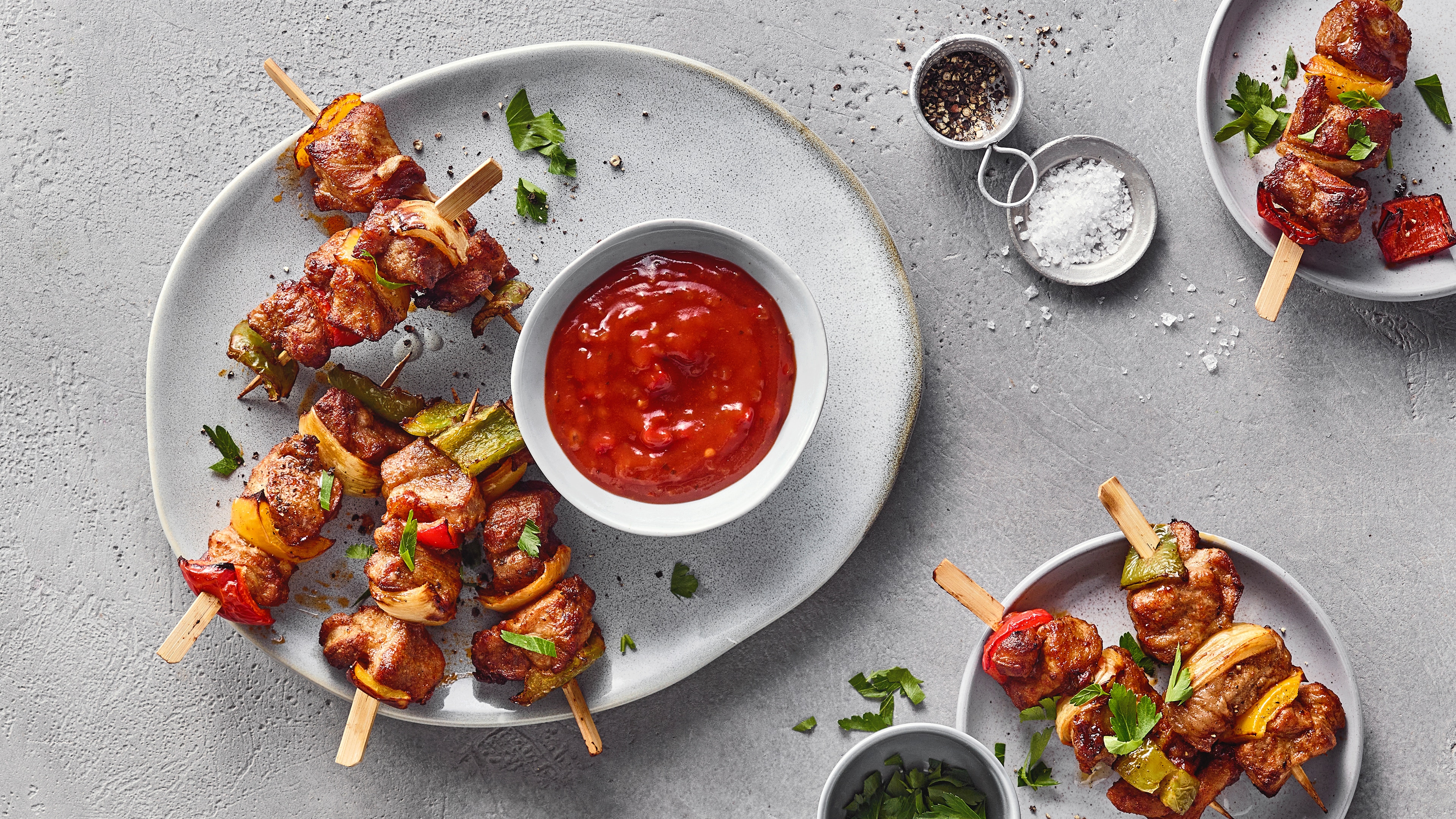 Ein Teller mit gegrillten Fleischspießen, roten, gelben und grünen Paprikastücken, Zwiebelstücken und einer Schale roter Soße.