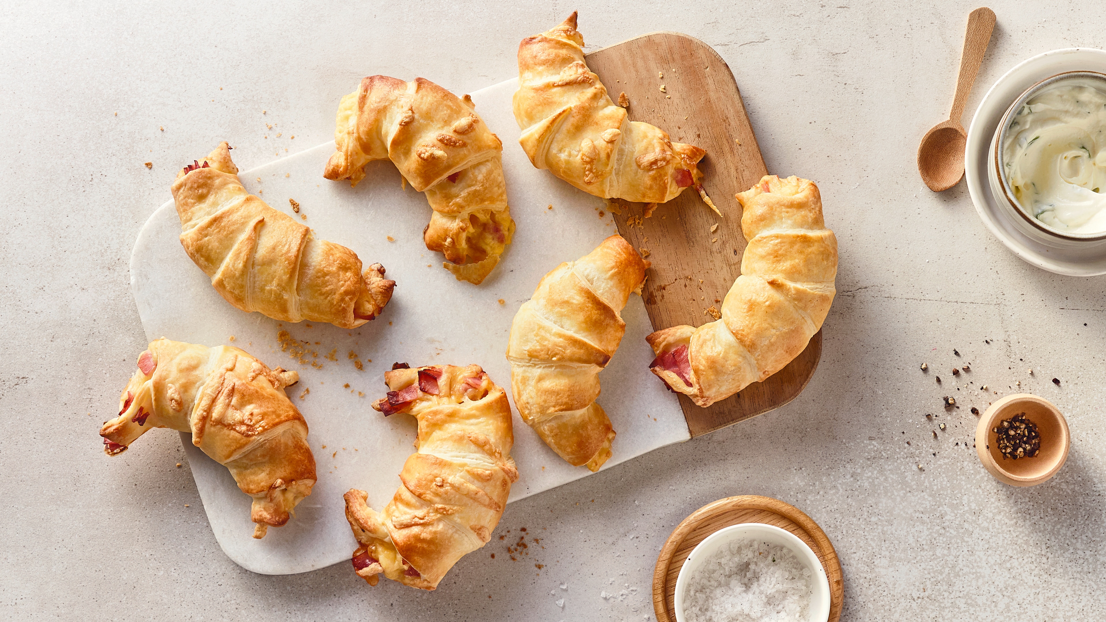 Rezept für Schinkenhörnchen Hörnchen aus gelbgoldenem Blätterteig, gefüllt mit Schinkenstückchen, auf einem rustikalen Holzbrett