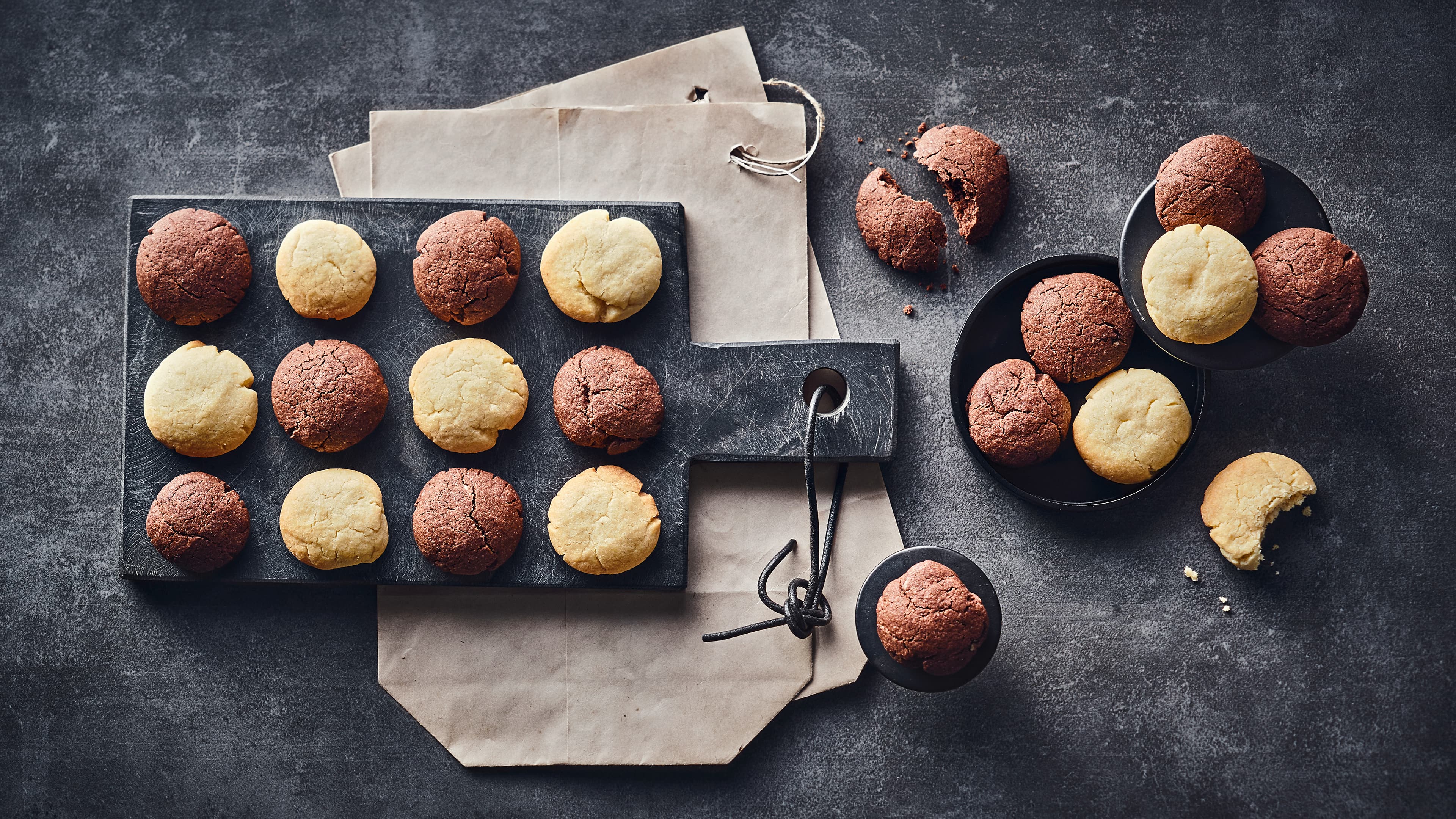 Keksrezept für Schmalznüsse Abwechselnd goldgelbe und schokobraune kleine, runde buttrige Kekse Auf einem dunklen Steinbrett